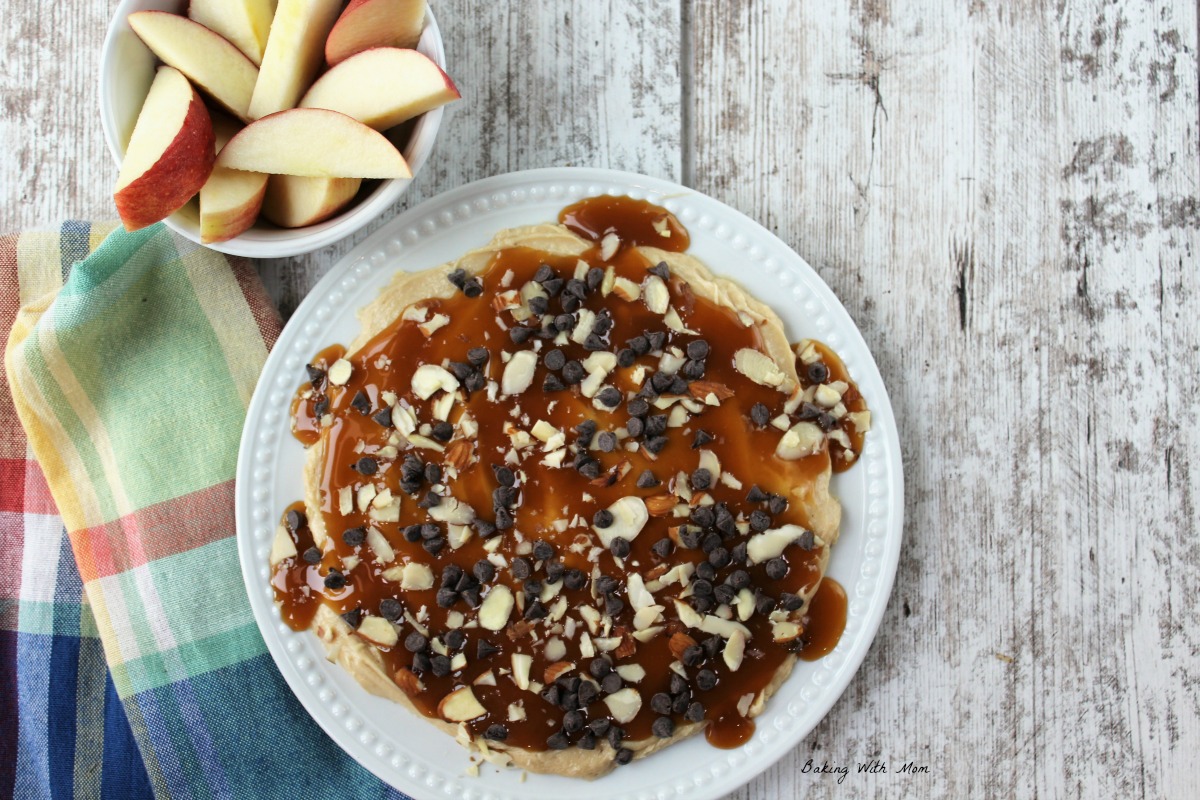 Plate of creamy caramel apple dip topped with chocolate chips, almonds on a white plate