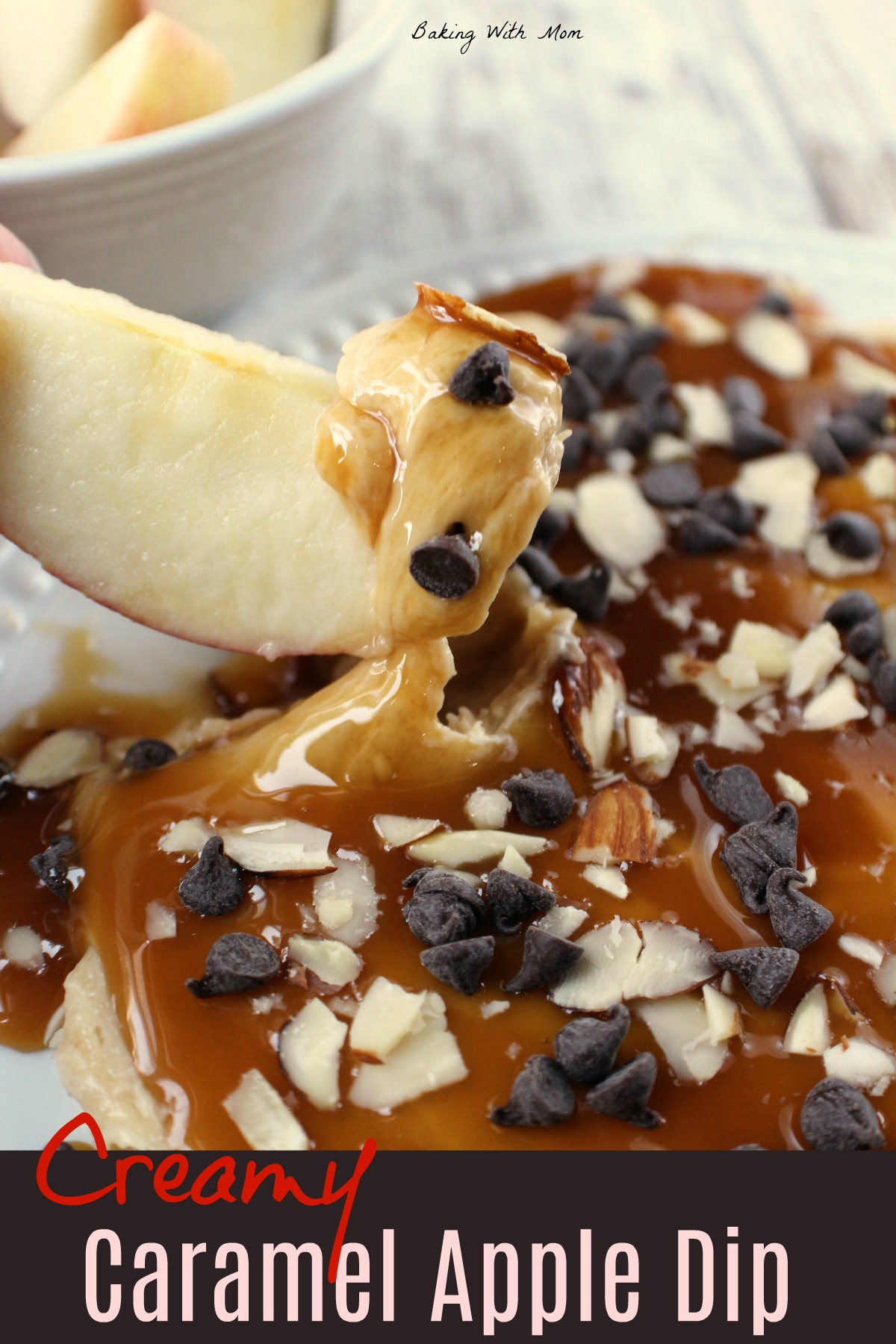 Apple slice with cream cheese dip on it and chocolate chips. A bowl of apples is sitting behind