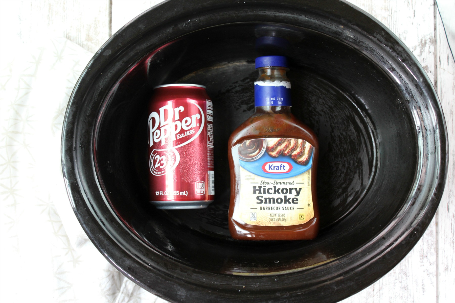 Crock pot with a can of Dr. Pepper and Hickory Smoke Kraft BBQ Sauce.