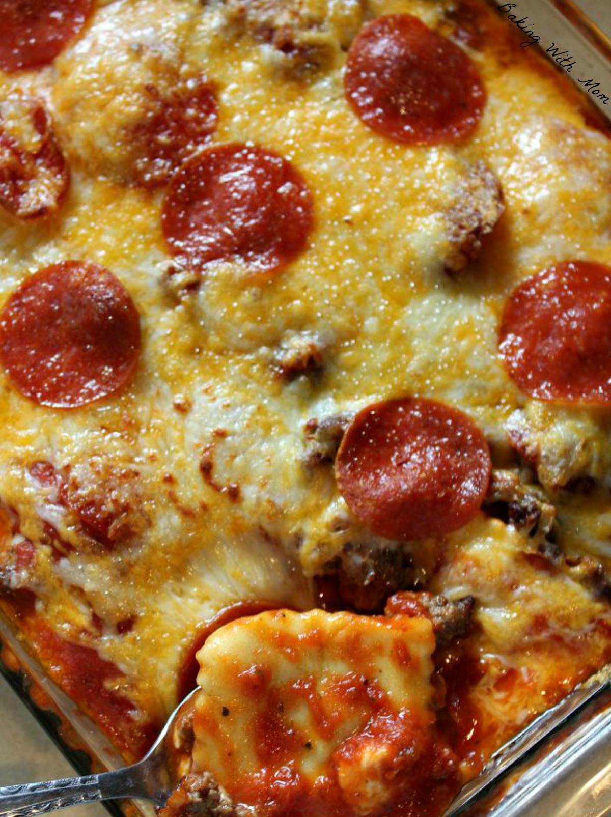 Pizza casserole with pepperoni and hamburger in a clear casserole dish and spoon nearby