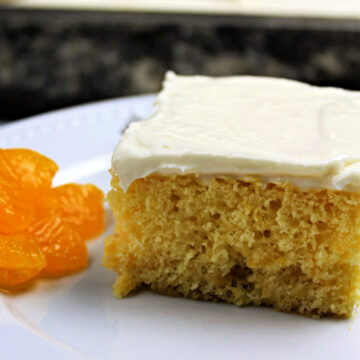 slice of orange cake with cream cheese frosting on a white plate with mandarin oranges