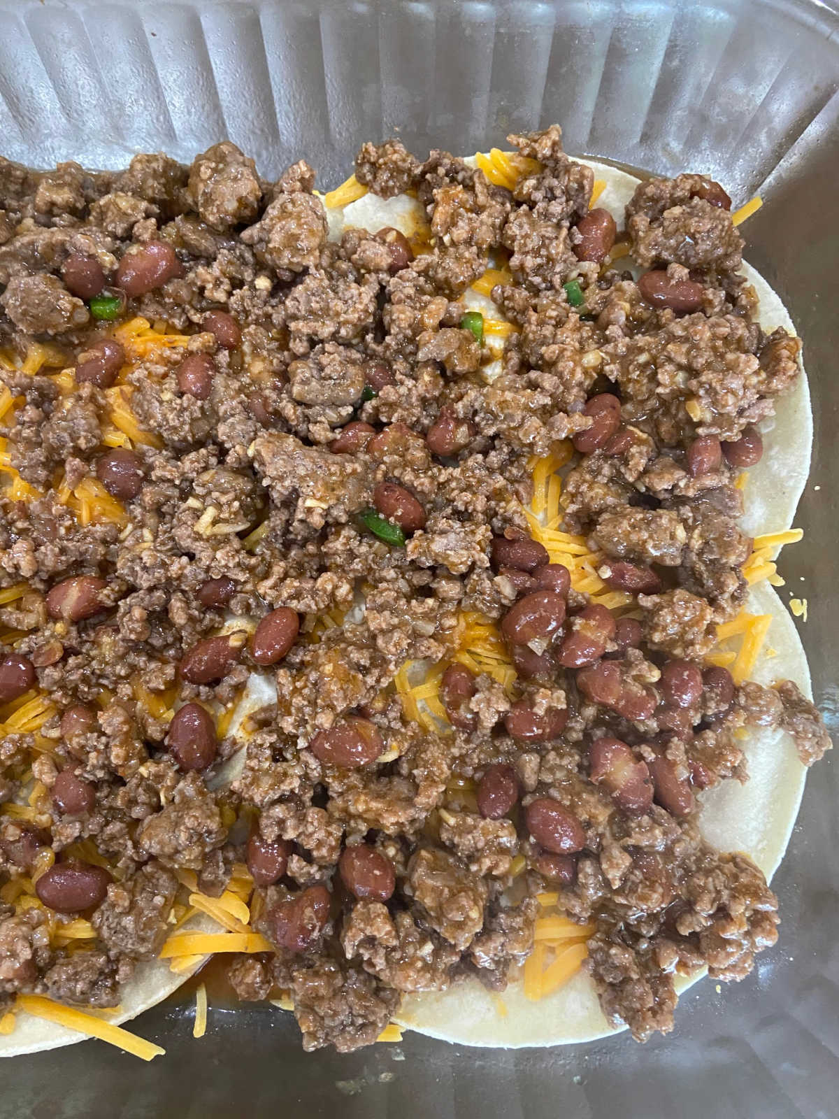 Casserole dish with corn tortillas, hamburger and beans and cheddar cheese