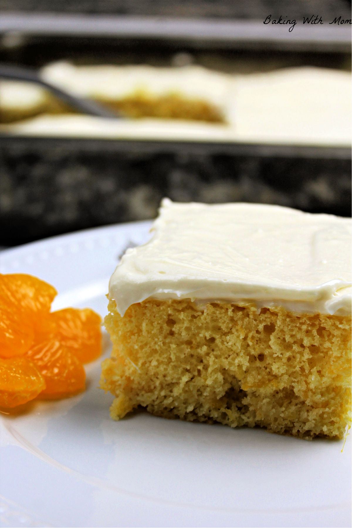 Slice of cake with mandarin oranges besides on a white plate.