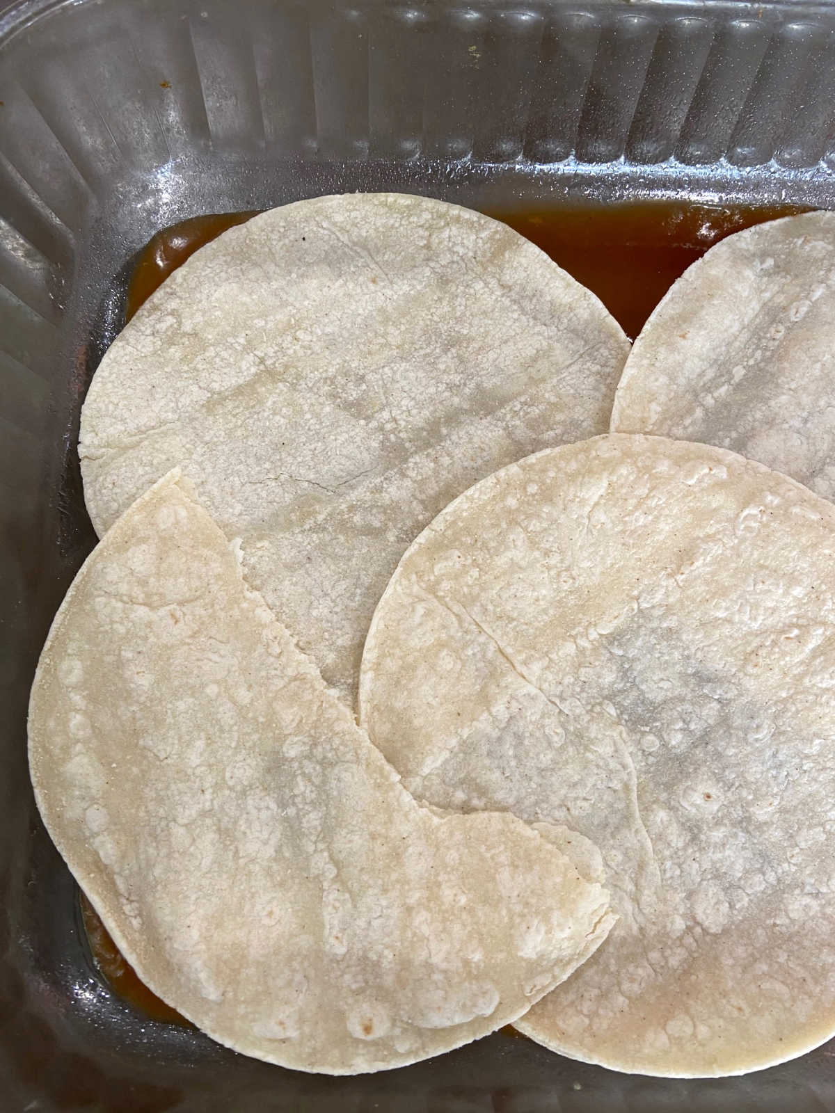 Casserole dish with red enchilada sauce and corn tortillas