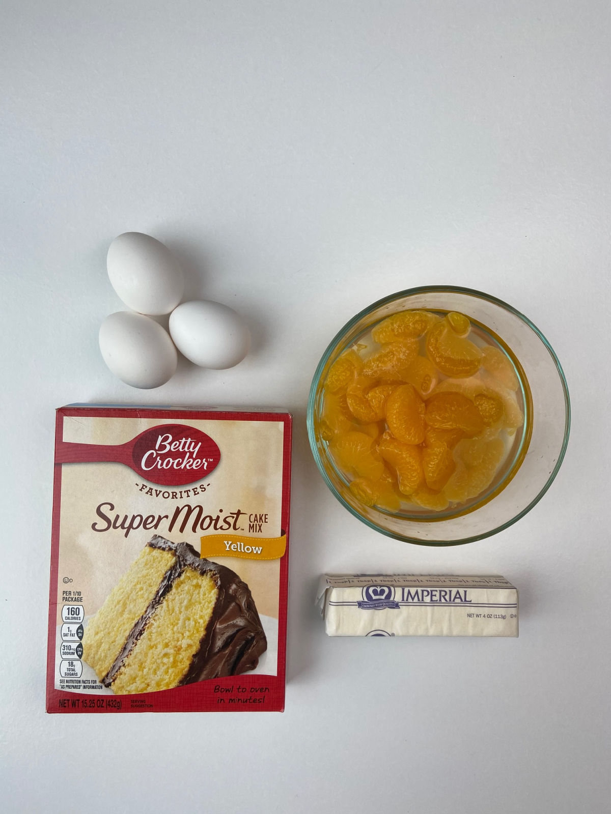 cake mix box, 3 eggs, mandarin oranges in bowl and stick of margarine