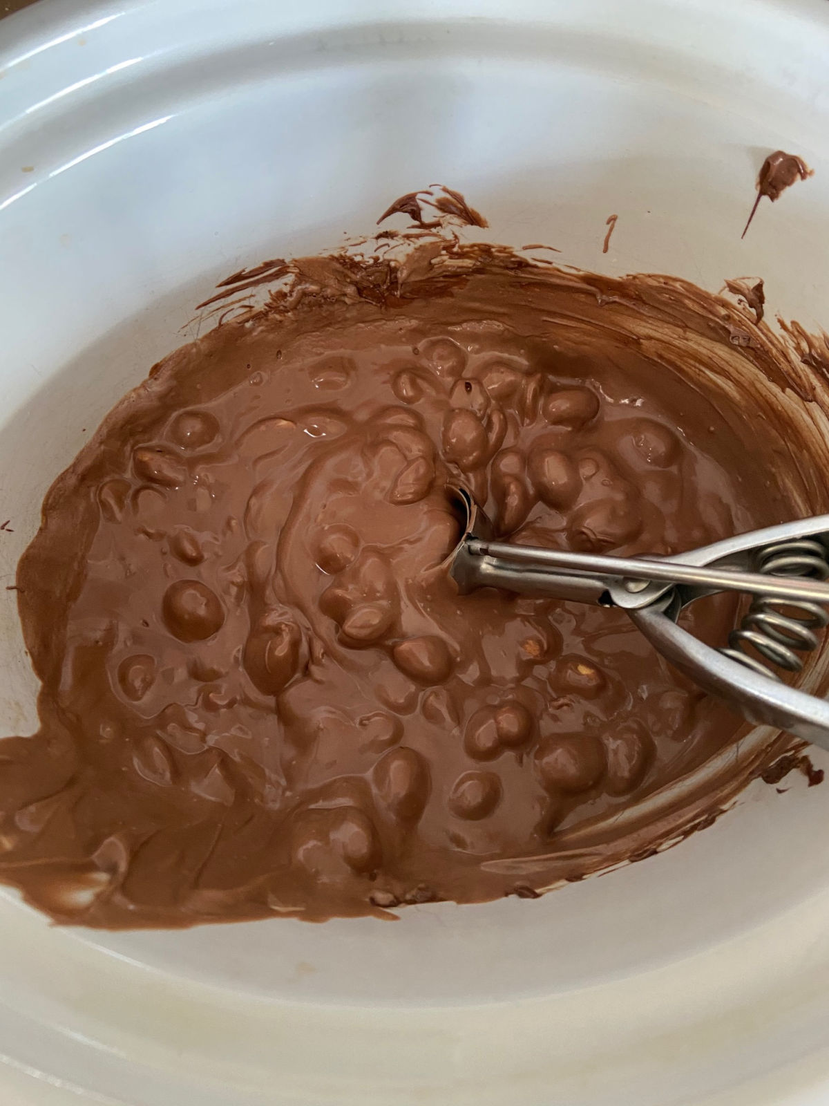 chocolate and peanuts in a crock pot with a scoop inside.