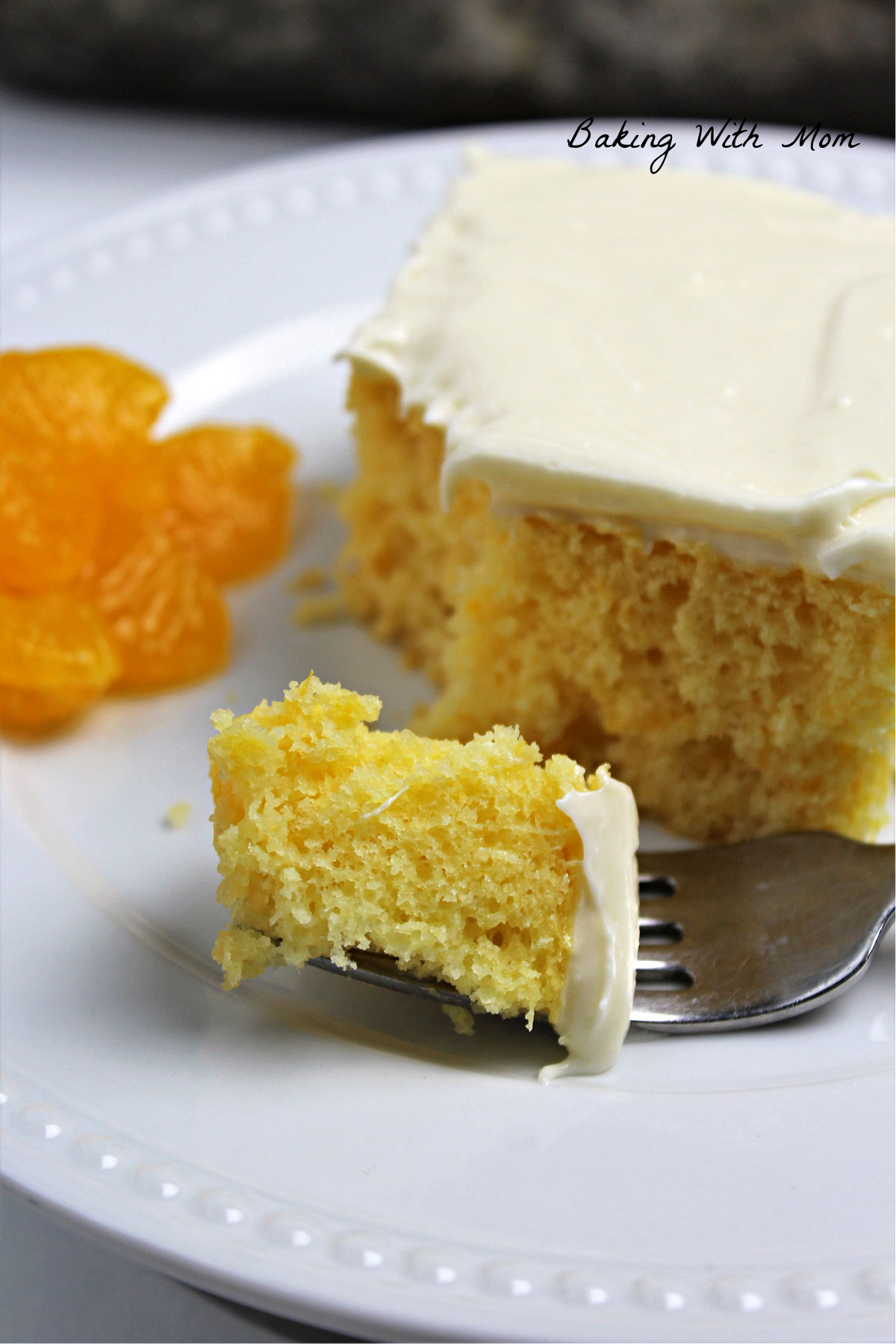 Fork with a piece of mandarin orange cake on it and slice of cake on a white plate.