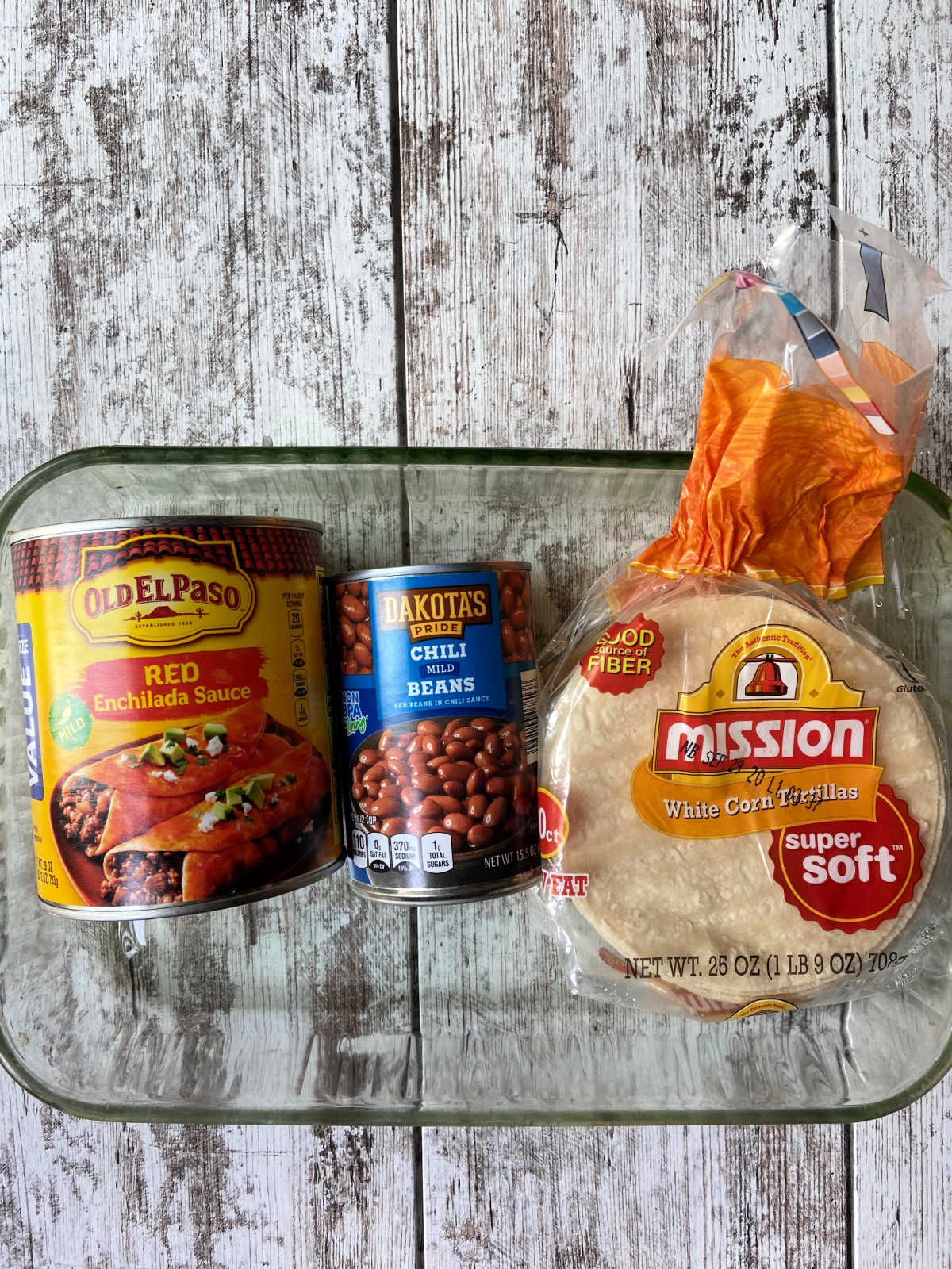 Casserole dish with enchilada sauce, chili beans and corn tortillas in their cans and packages