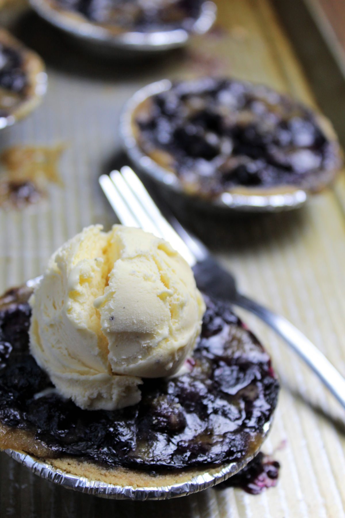 mini blueberry pies on a cooking sheet with a scoop of vanilla ice cream on top of one pie