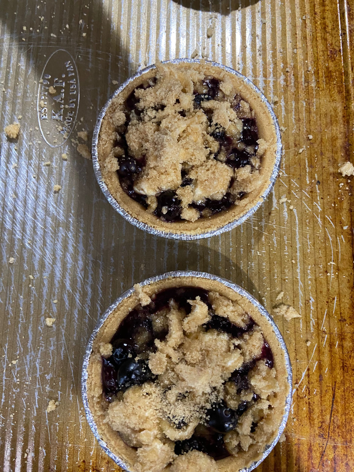 Mini pies on a cooking sheet with uncooked blueberry filling inside. 