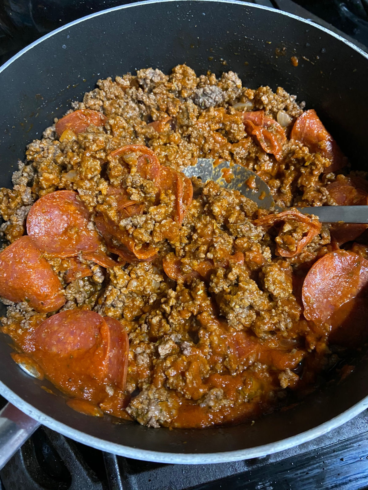 Cooked hamburger with pepperoni and pizza sauce in a frying pan. 