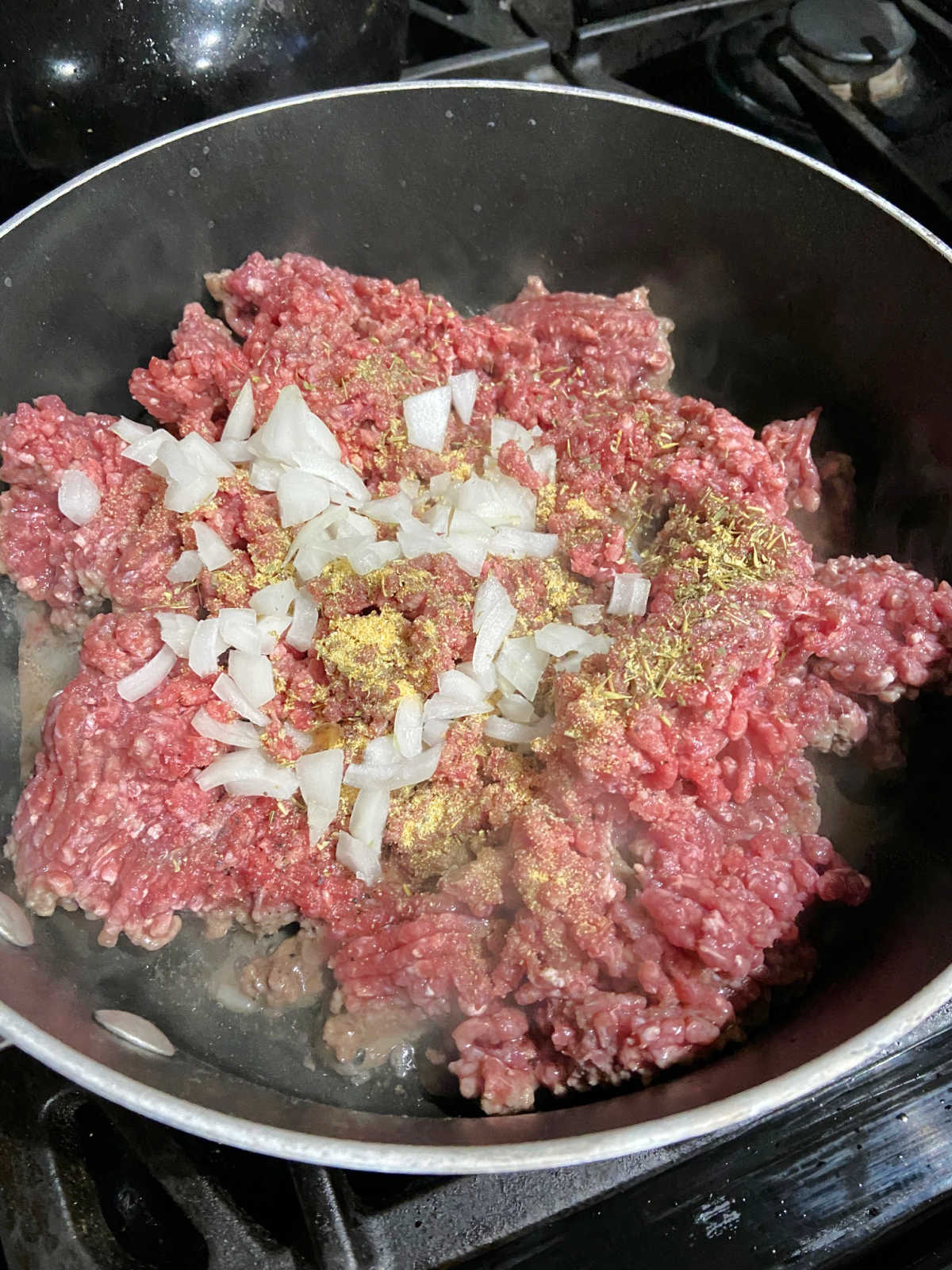 Ground beef cooking in a frying pan with diced onions on top.