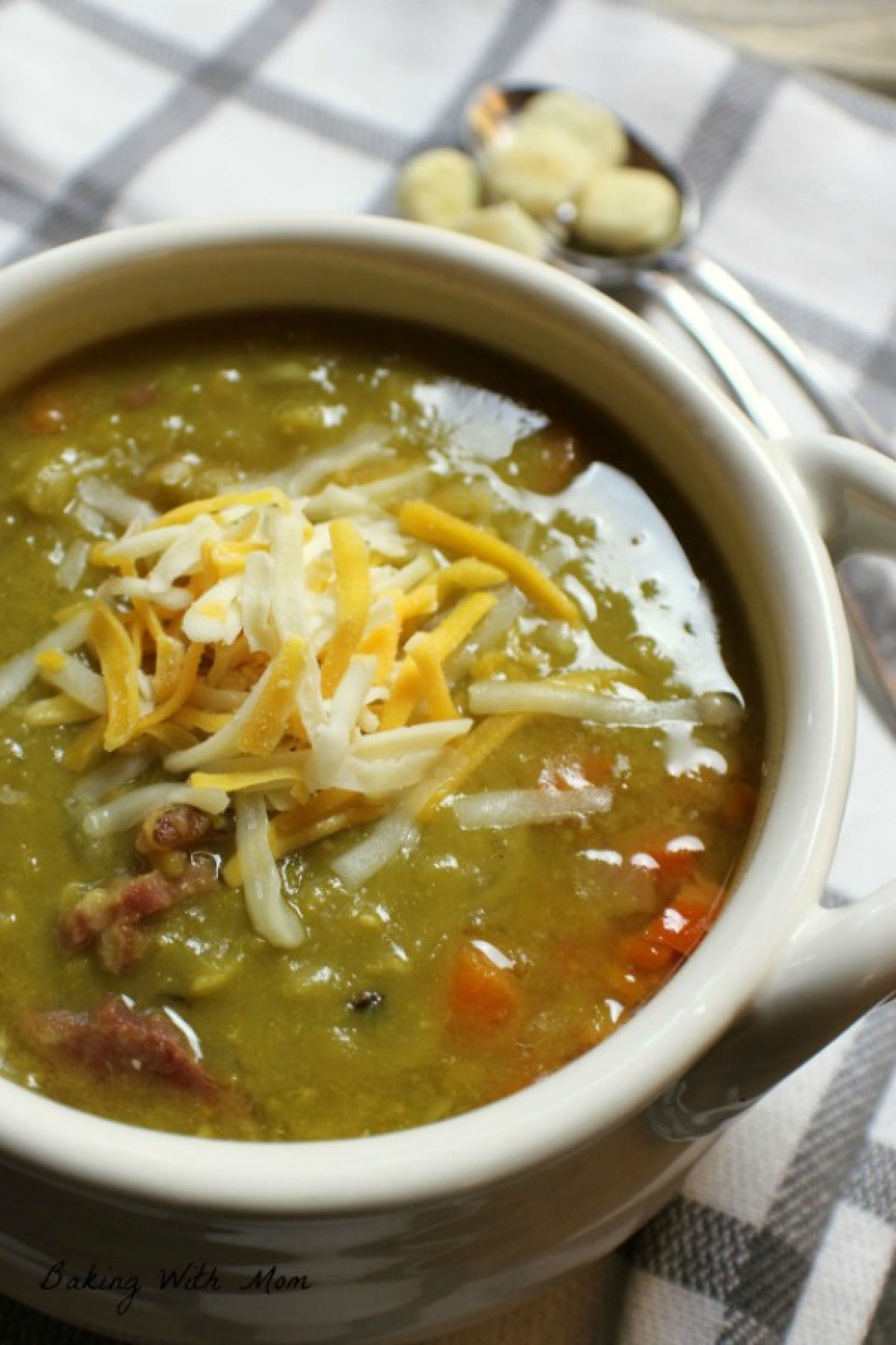 Pea soup in a white bowl with crackers laying besides. 