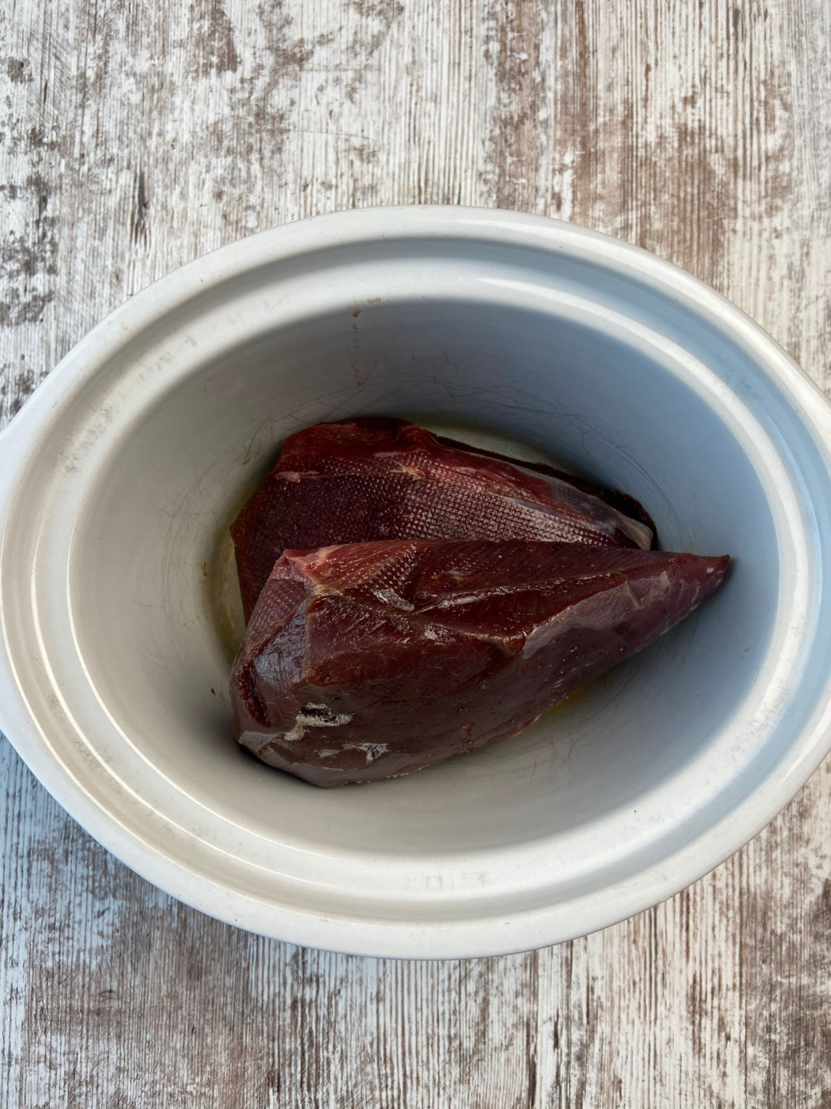 Fresh raw venison roast in a white crock pot.