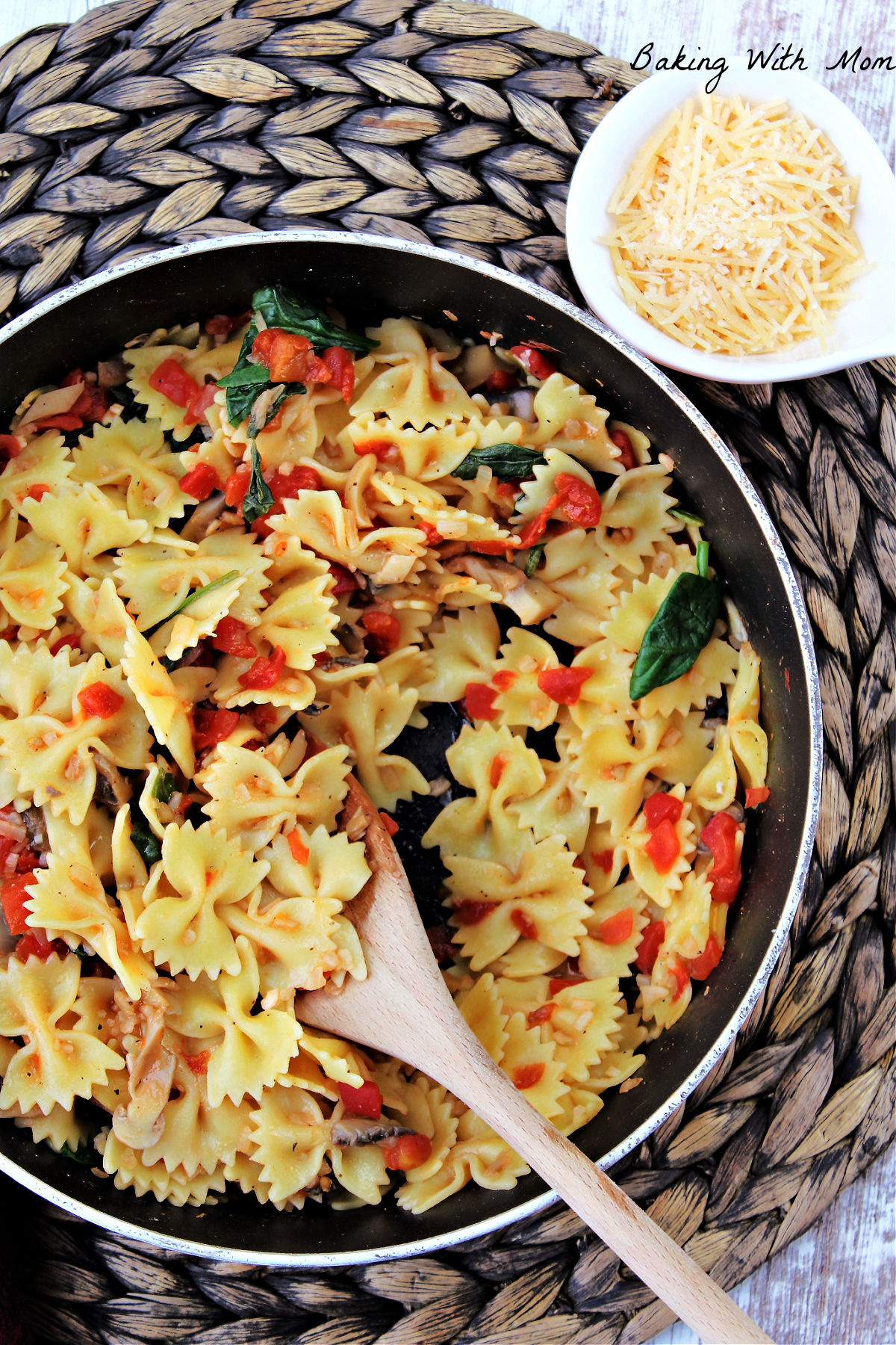 bow tie pasta with spinach, tomatoes and mushrooms in a frying pan and parmesan cheese besides.  