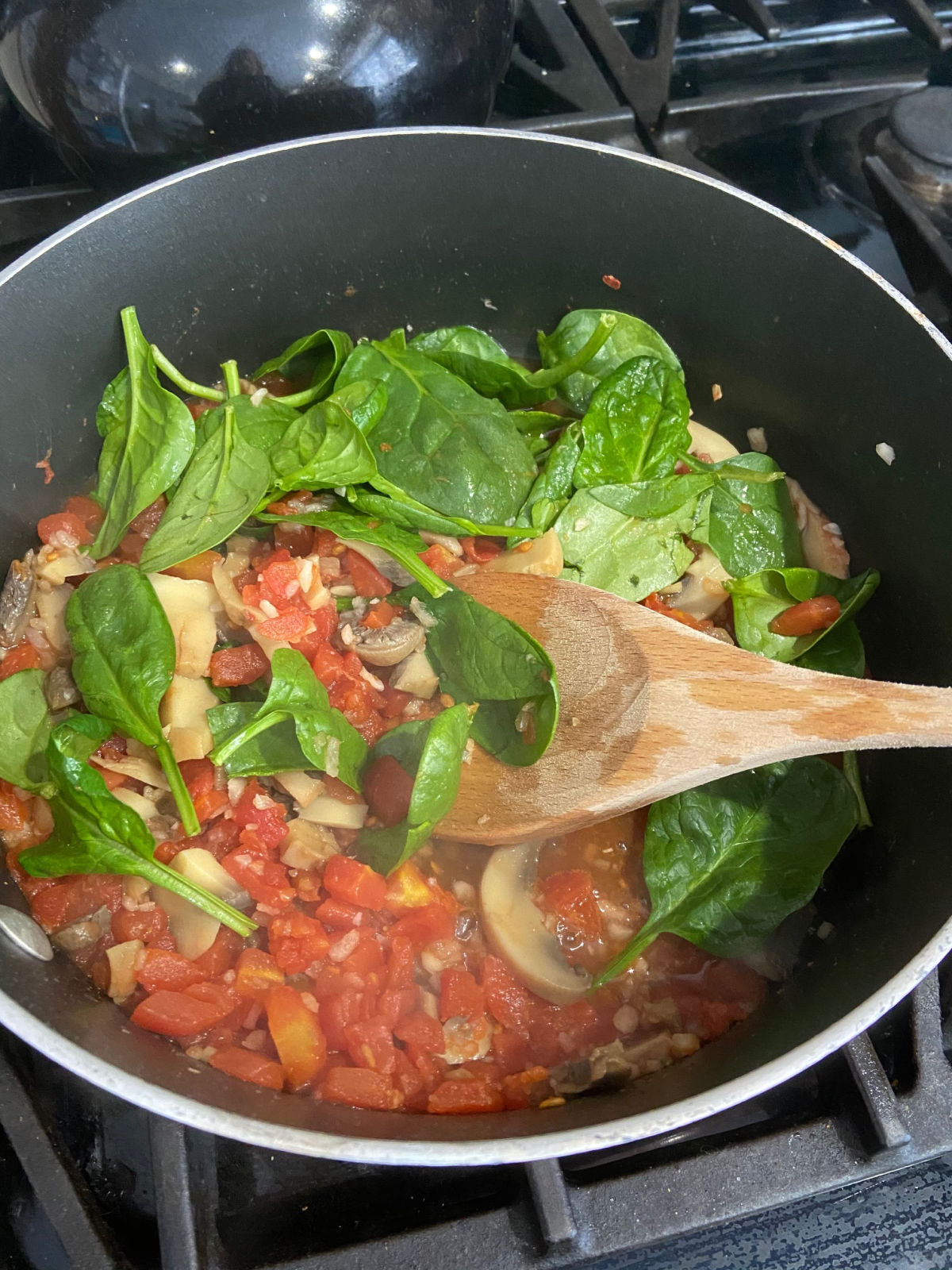 fresh spinach in a frying pan with tomatoes and mushrooms. 