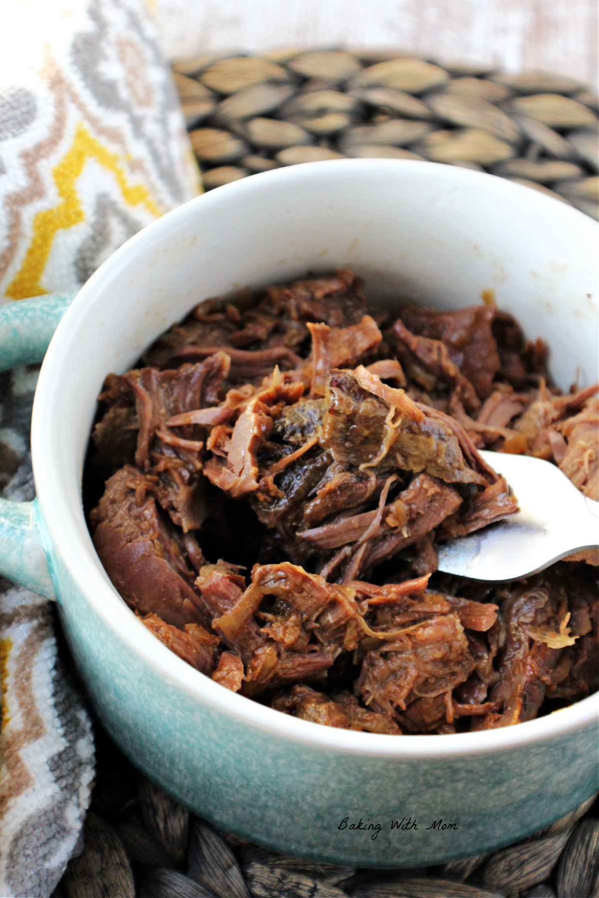 Deer roast in a gray bowl with a fork holding some pieces of meat. 