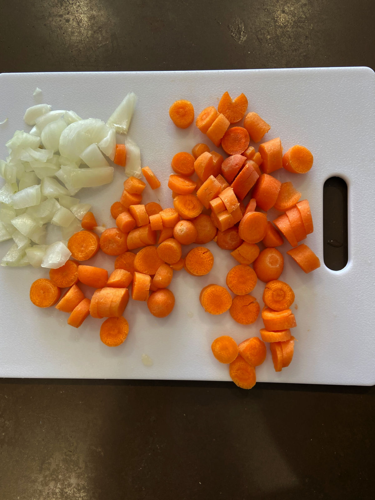 chopped carrots and onions on a white cutting board.