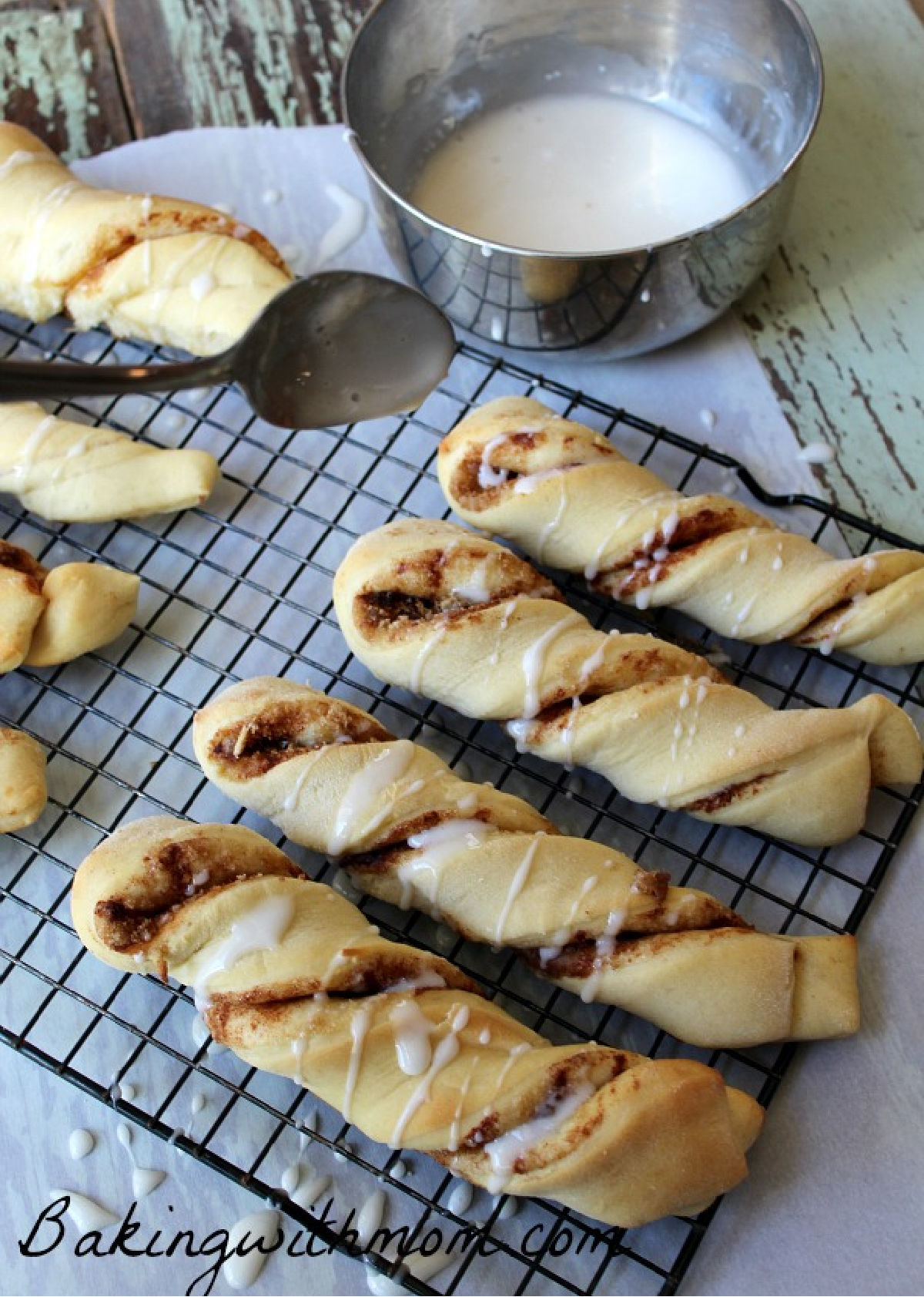 Cinnamon twists on a cooling rack being drizzled with frosting. 