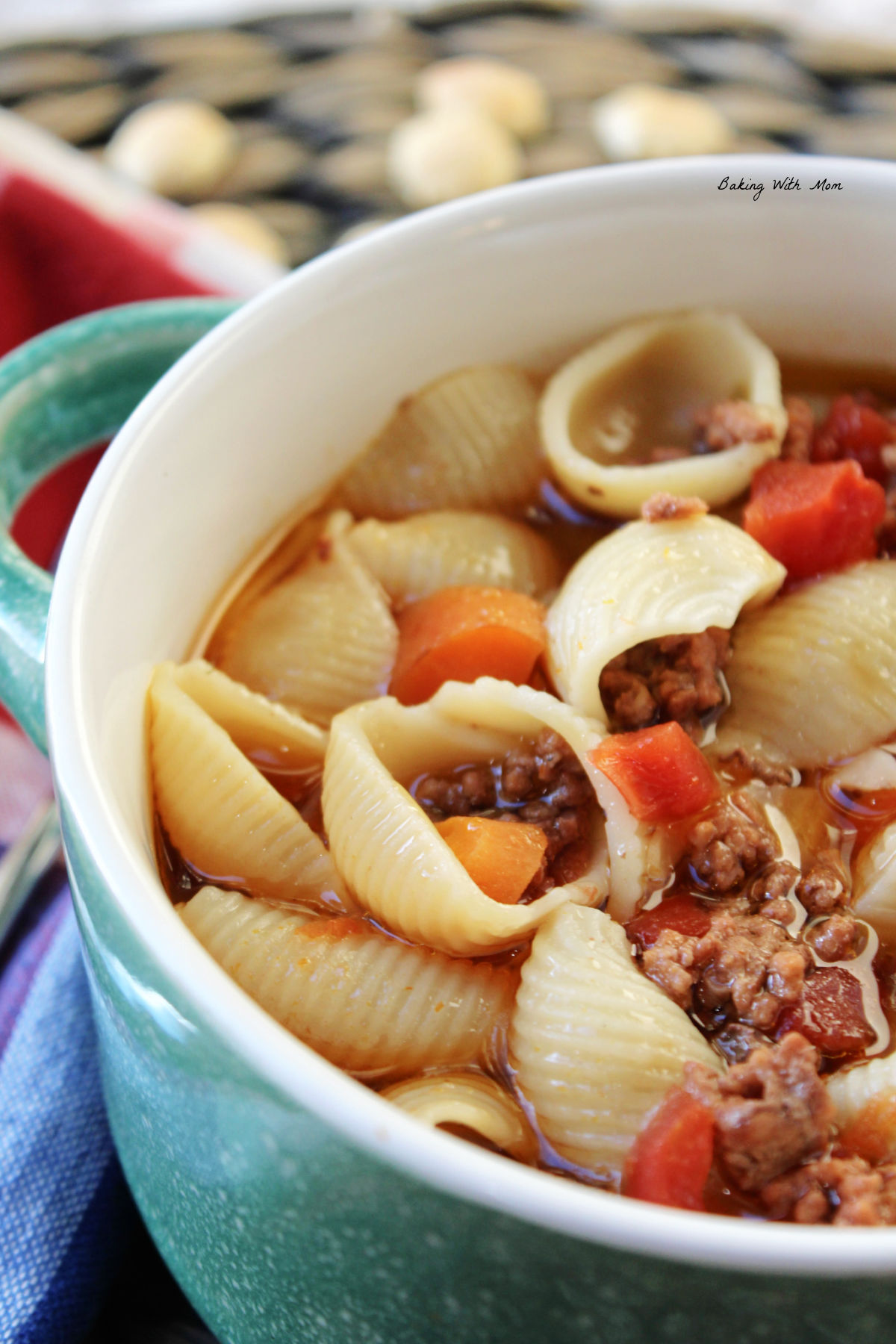 Hamburger soup in a blue bowl with shells, hamburger, carrots and tomatoes. 