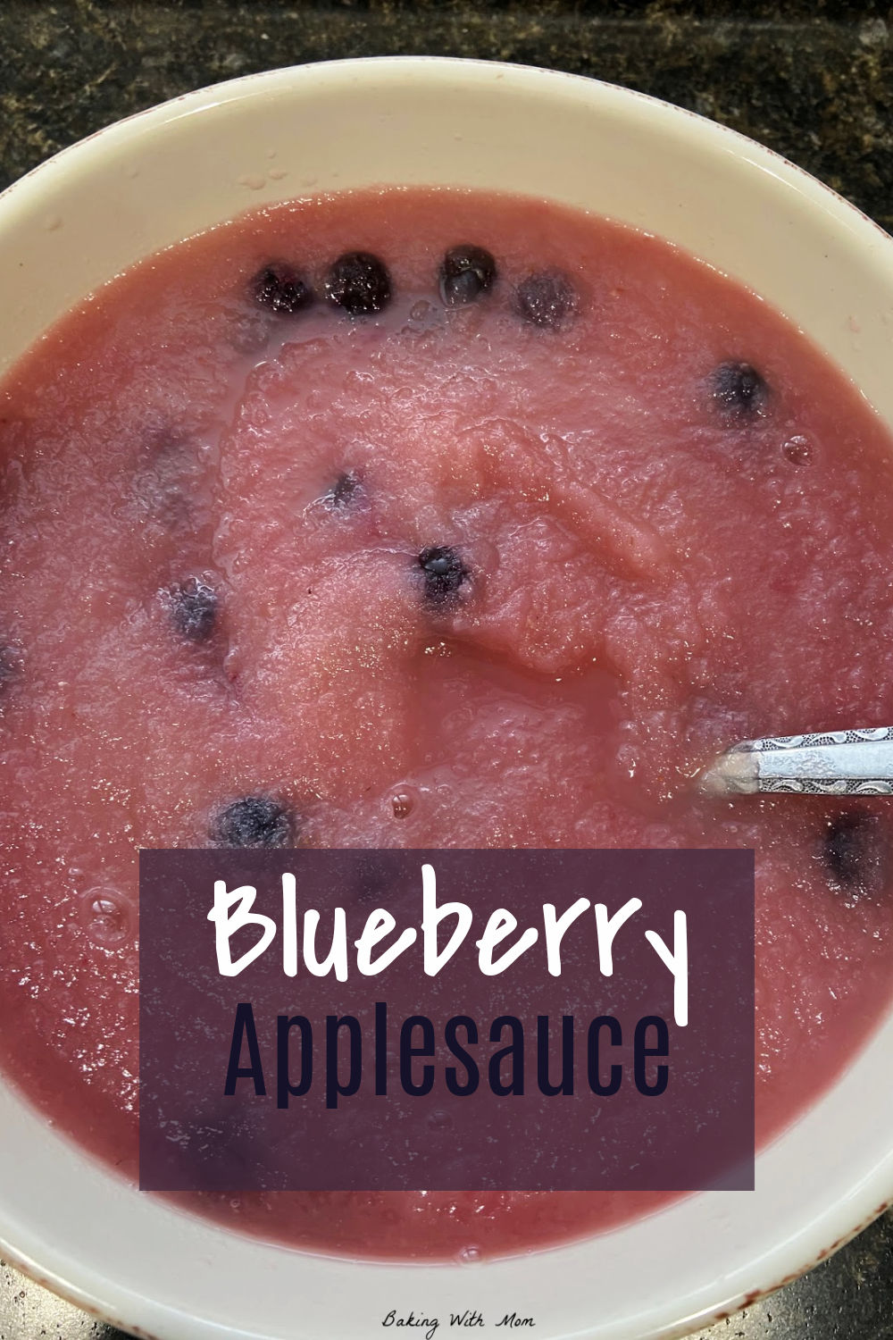 Blueberry applesauce with a spoon in a cream colored bowl. 