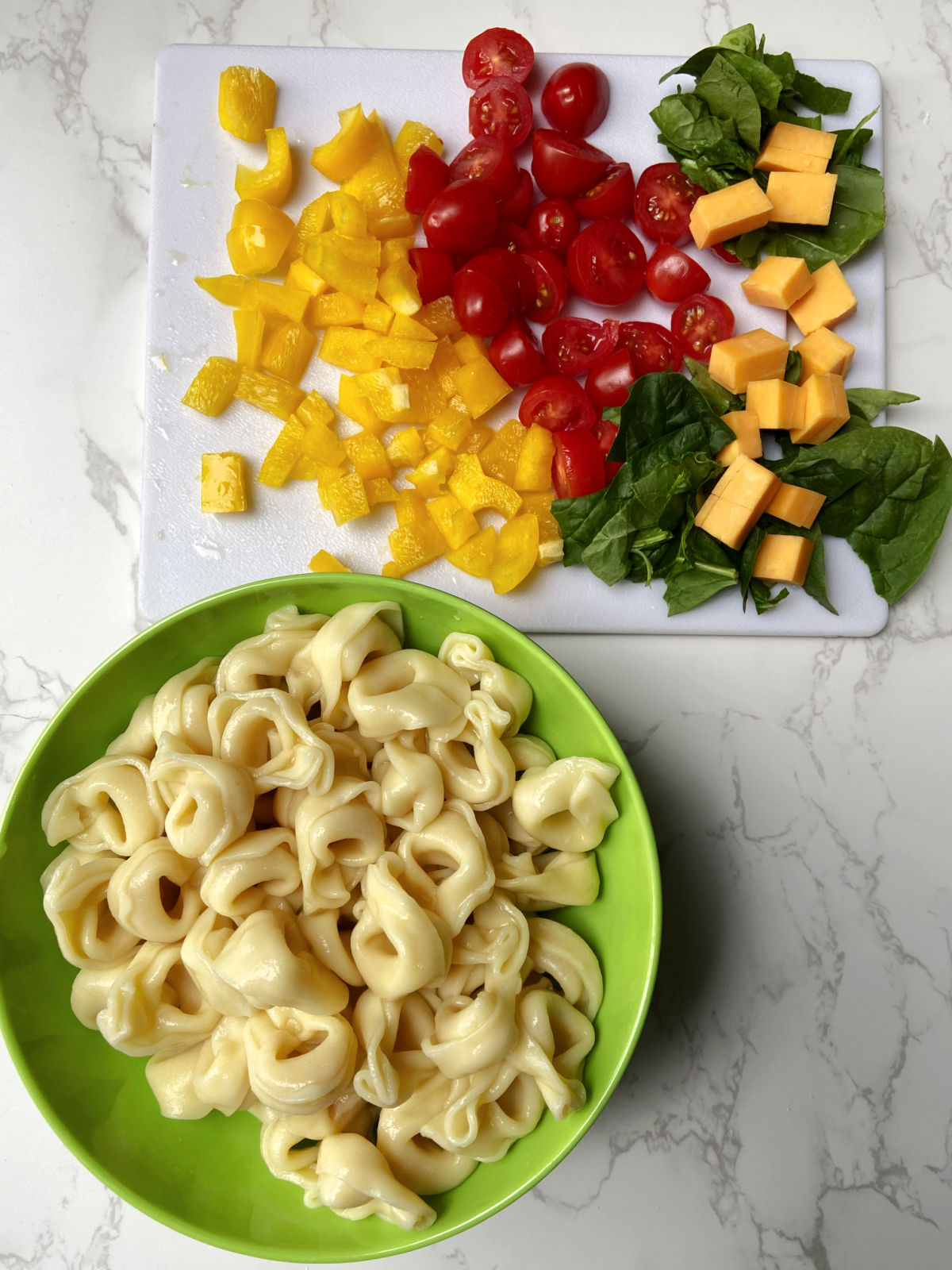 Bowl of cooked tortellini and chopped peppers, spinach, tomatoes and cheese. 