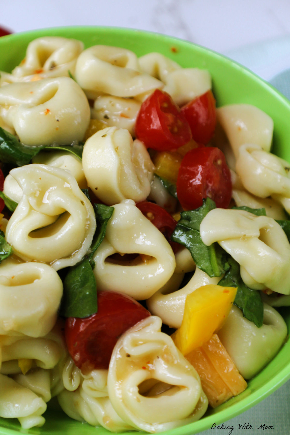 Bowl of tortellini salad with tomatoes and spinach.