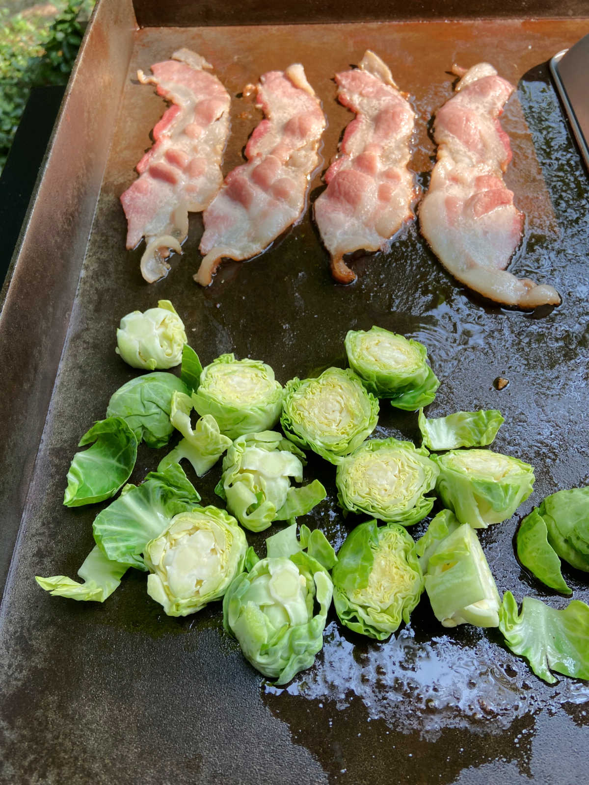 Bacon and brussels sprouts on a flat top grill cooking. 