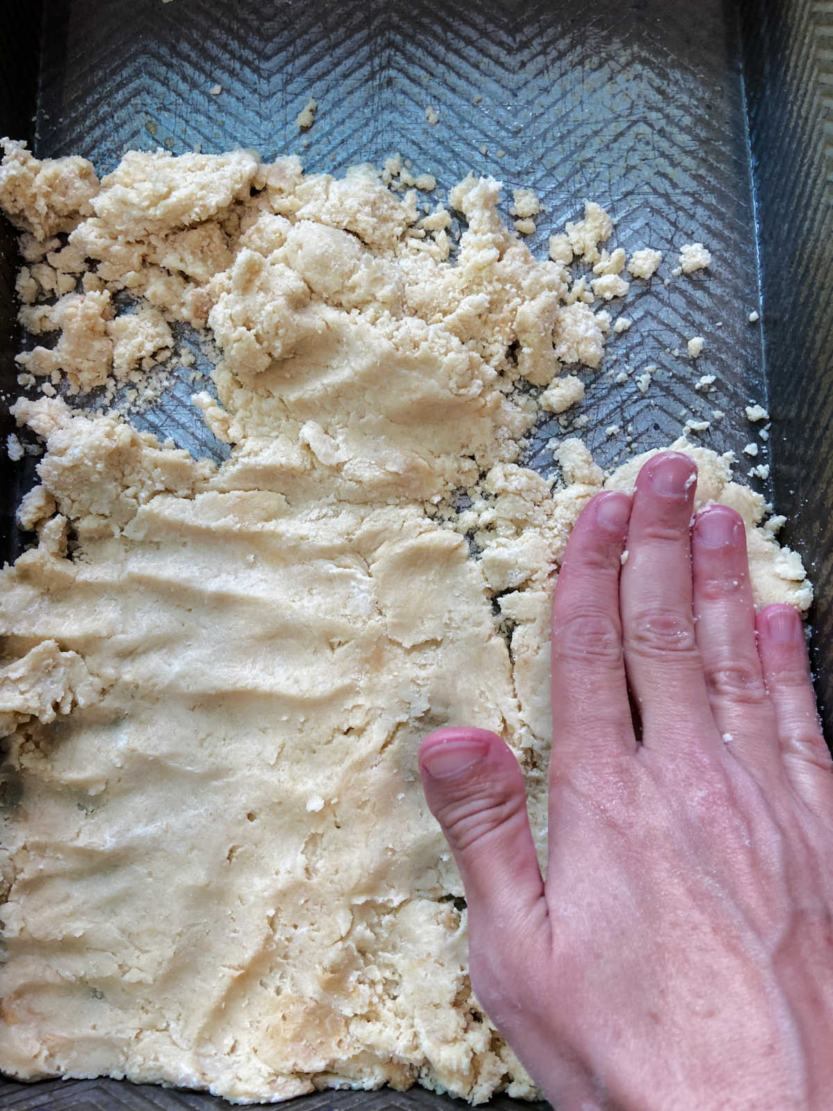 A hand flattening shortbread in the bottom of a pan. 