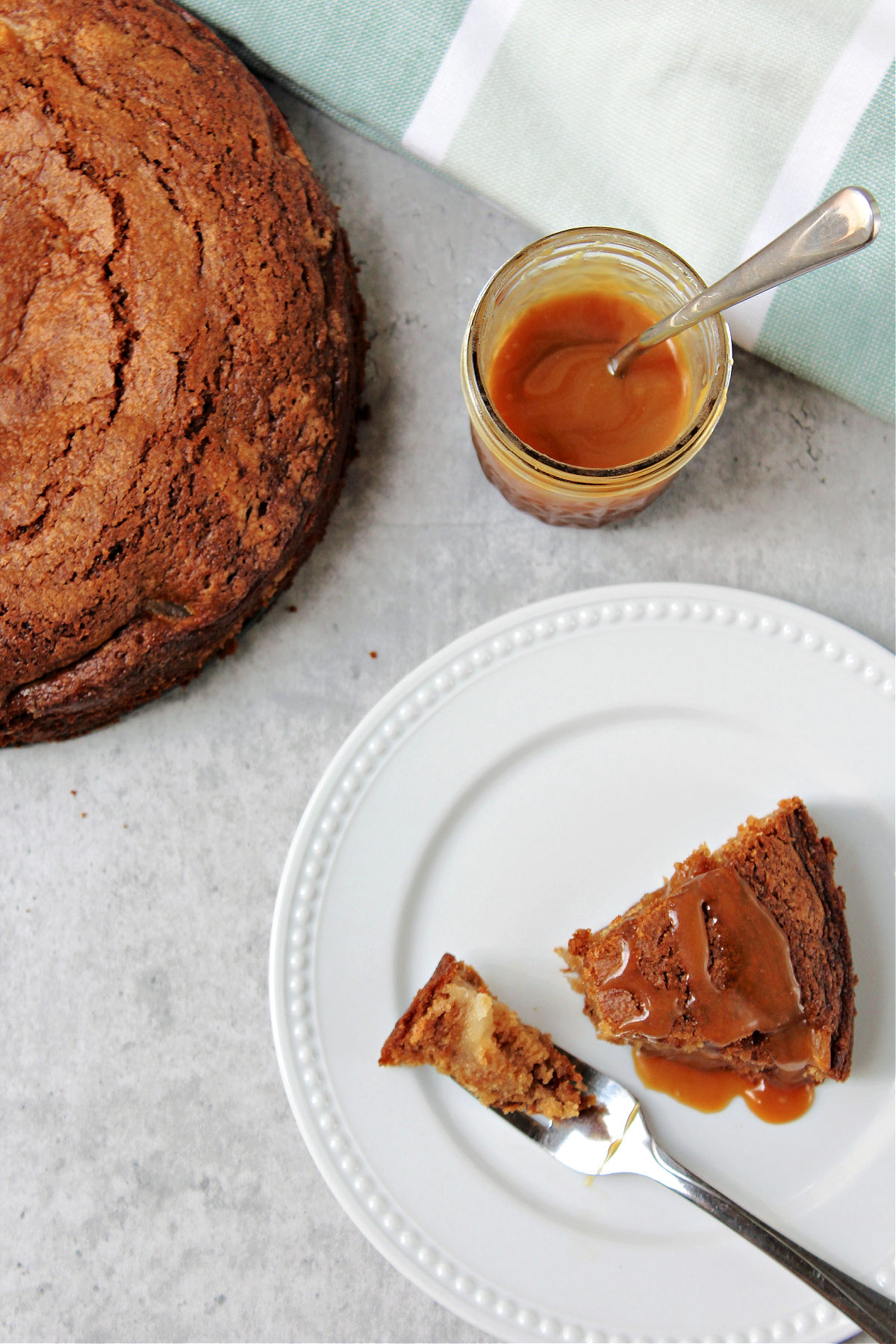Apple cake whole and slice with homemade caramel nearby. 