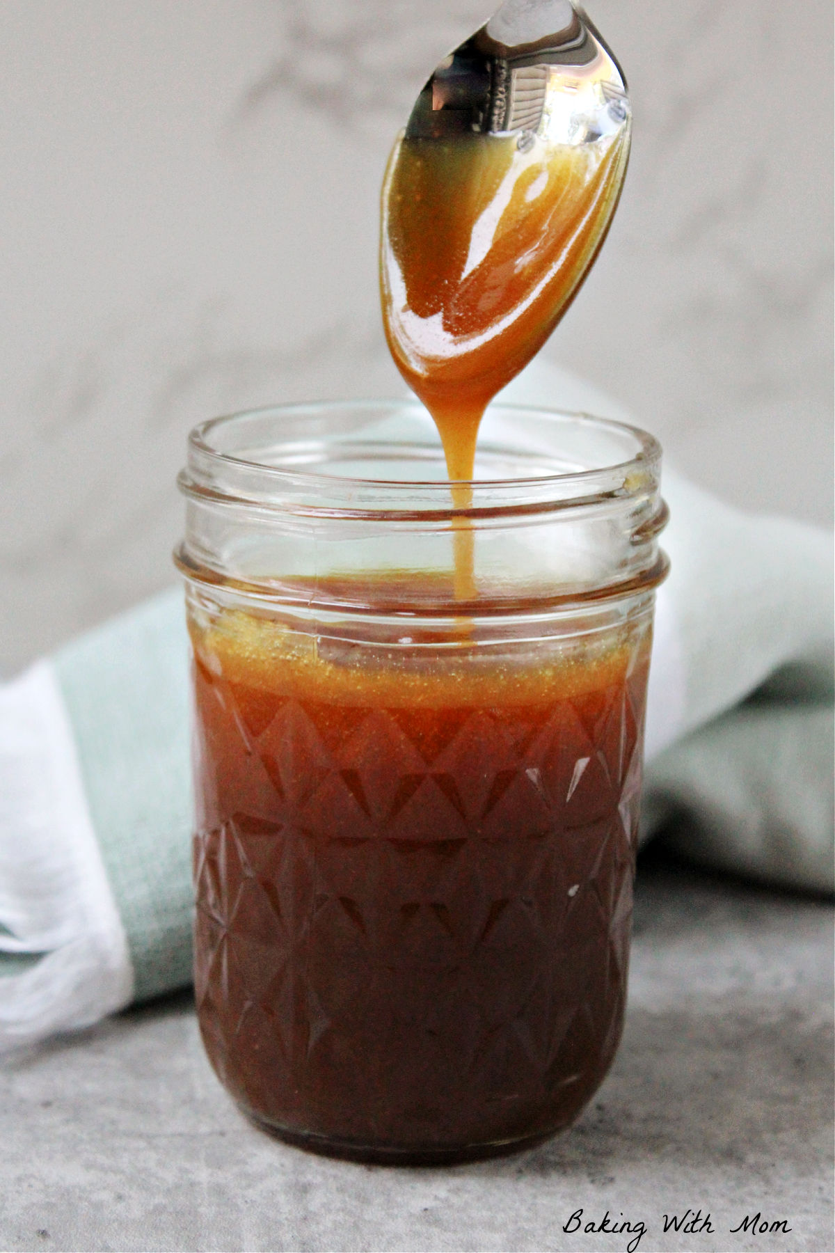 caramel sauce in a jar with a spoon lifted out of the sauce. 