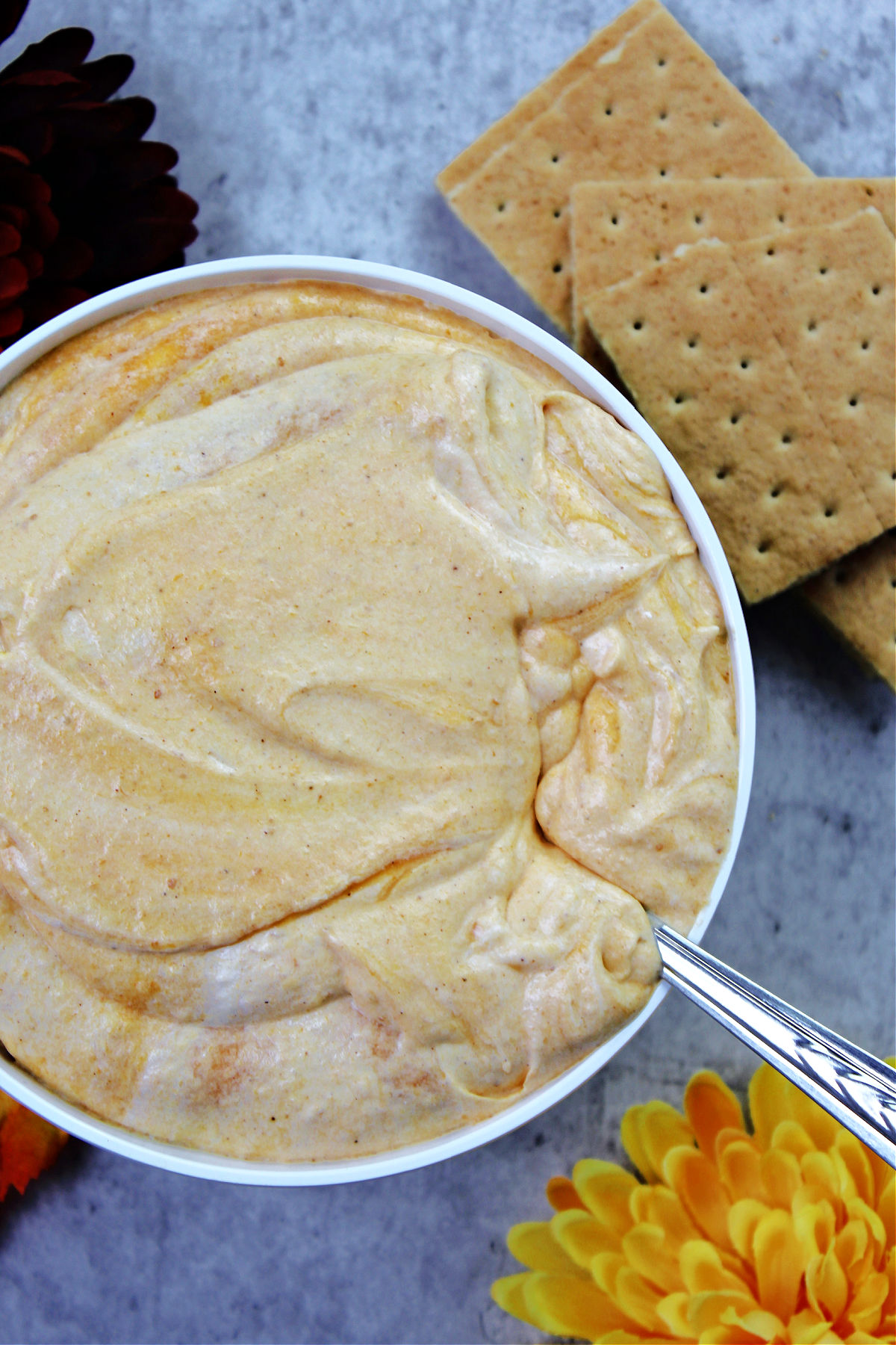 bowl of pumpkin pie dip with a spoon and flowers.