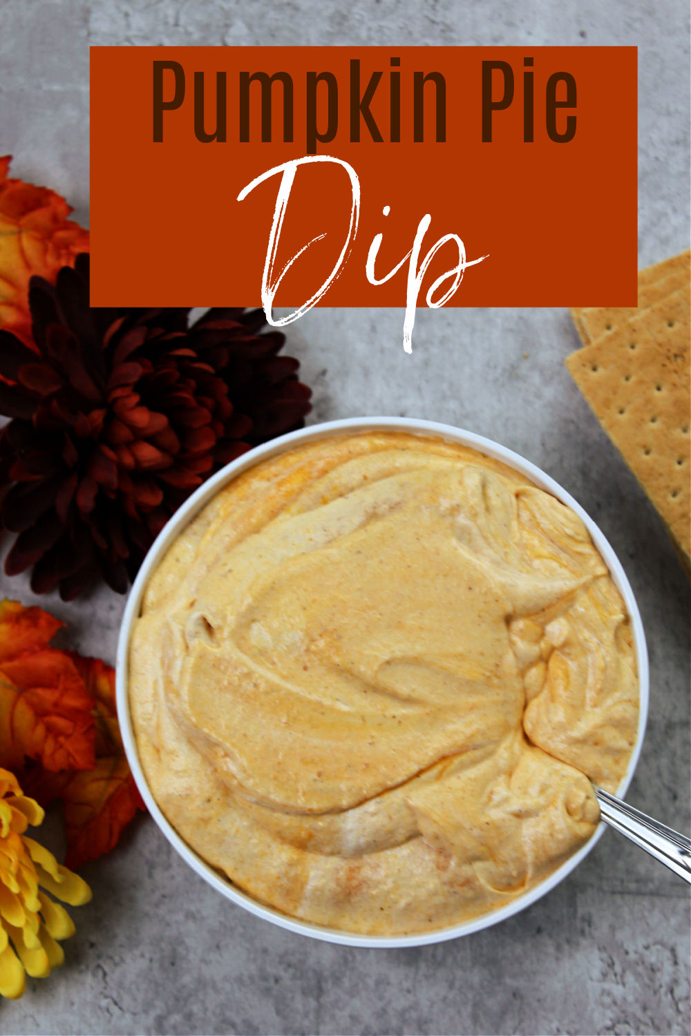 bowl of pumpkin pie dip with a spoon, flowers and crackers nearby. 