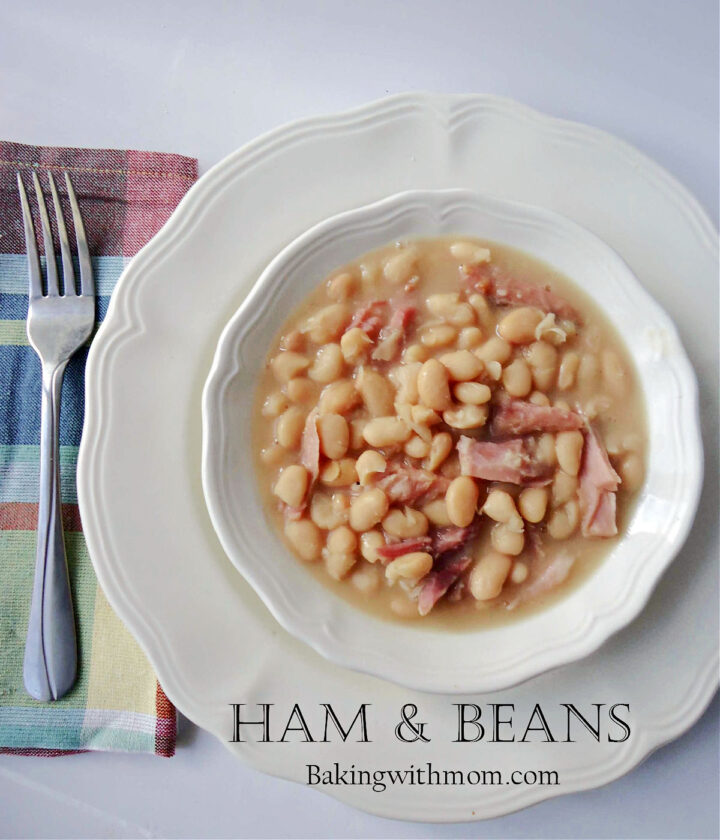 ham and beans in a white bowl with a white plate underneath. 