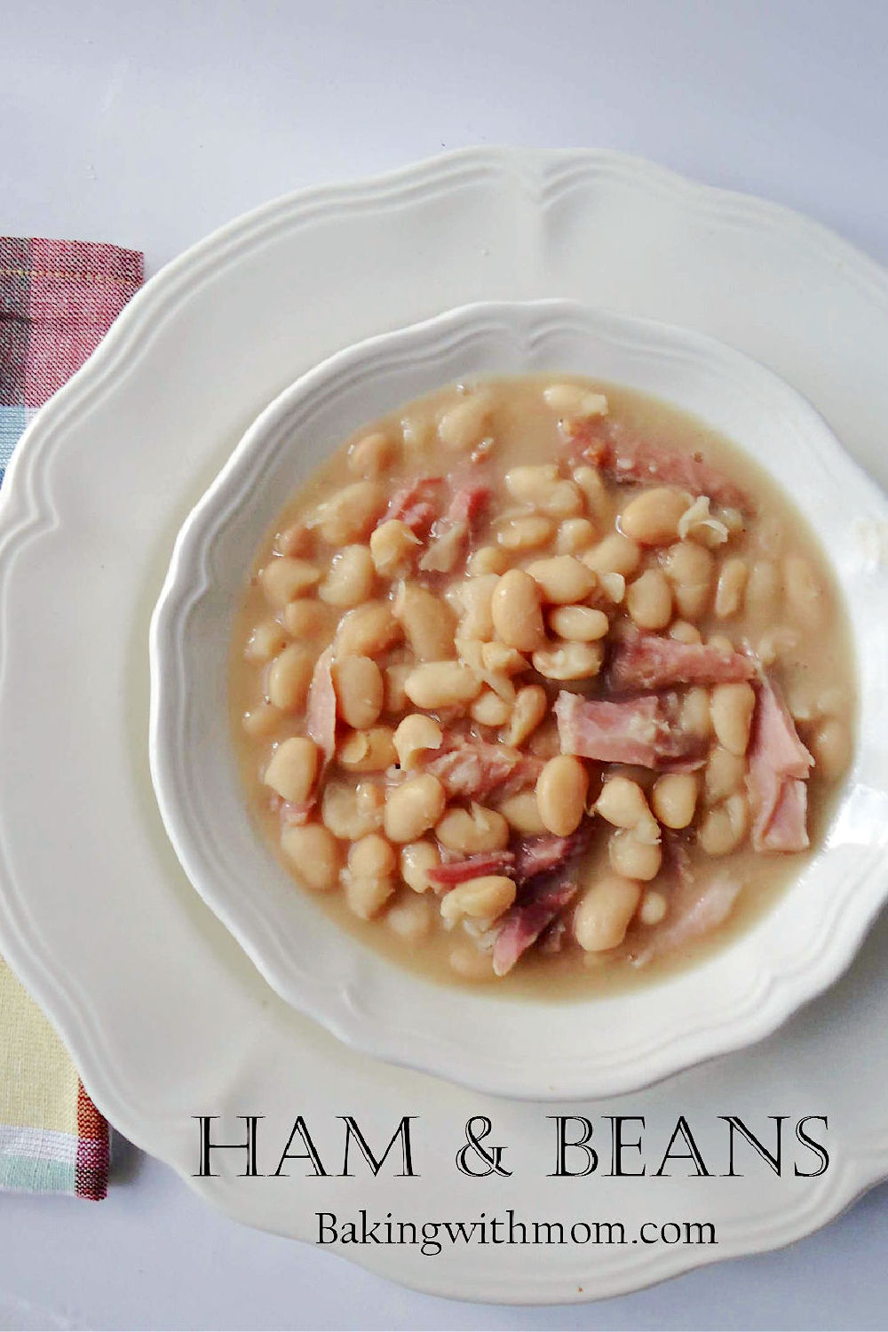 Ham and beans in a white bowl with a white plate under it. 