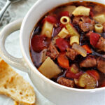 sausage soup in a bowl and bread beside.