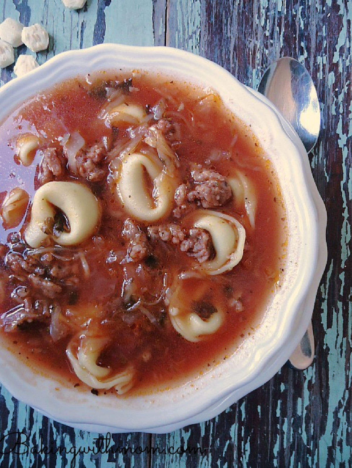 Bowl of spicy sausage tortellini soup in a white bowl.  