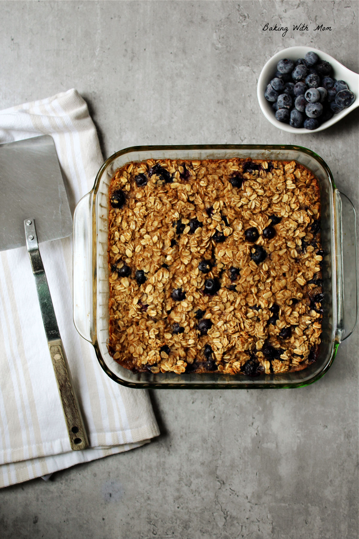 Blueberry baked oatmeal in a square baking dish with a spatula laying besides. 