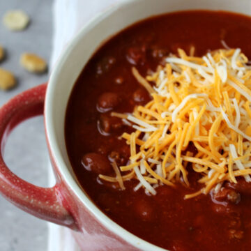 venison chili in a red bowl with cheese on top