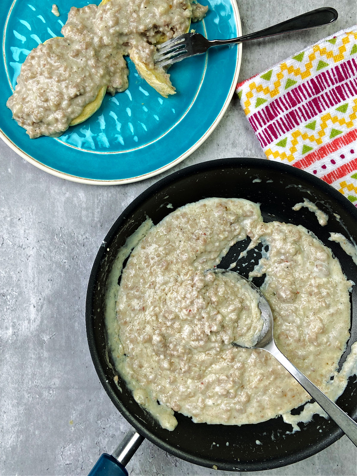 Sausage gravy in a frying pan with a silver serving spoon inside. 