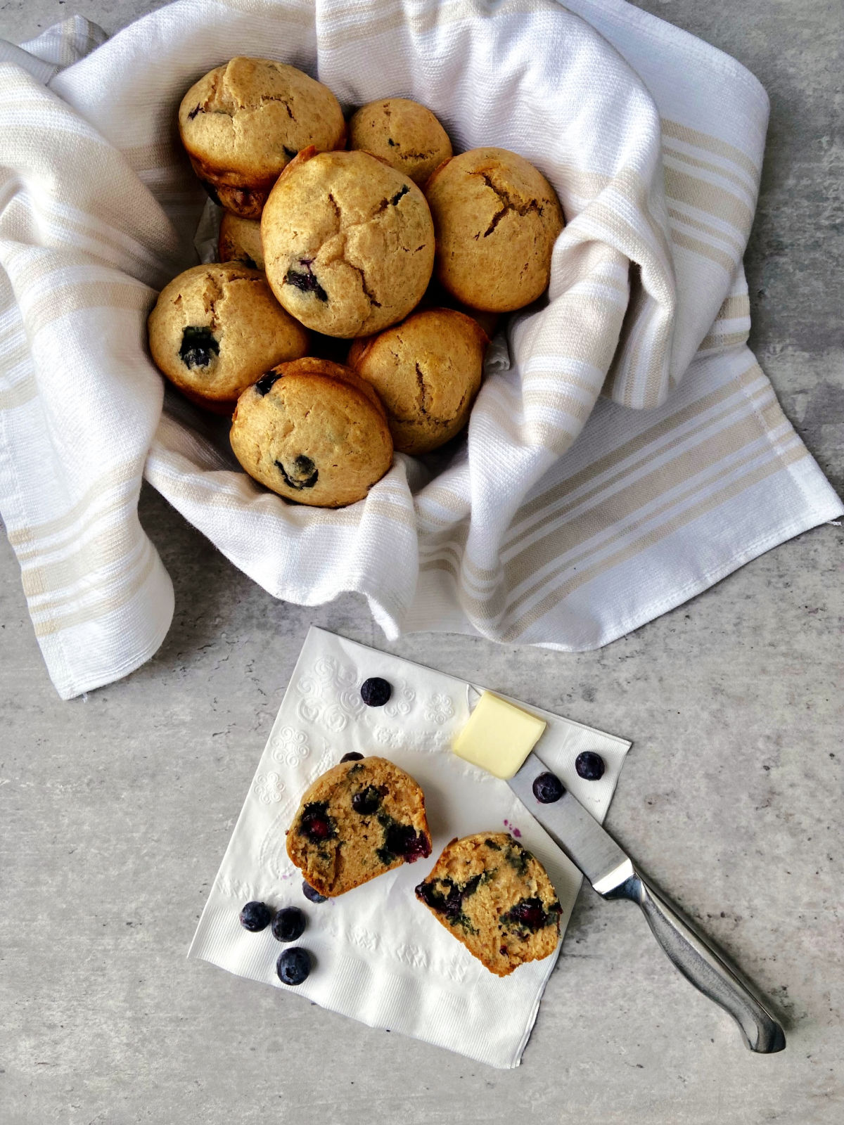 A bowl of sugar free blueberry muffins with a cut blueberry laying on a napkin. 