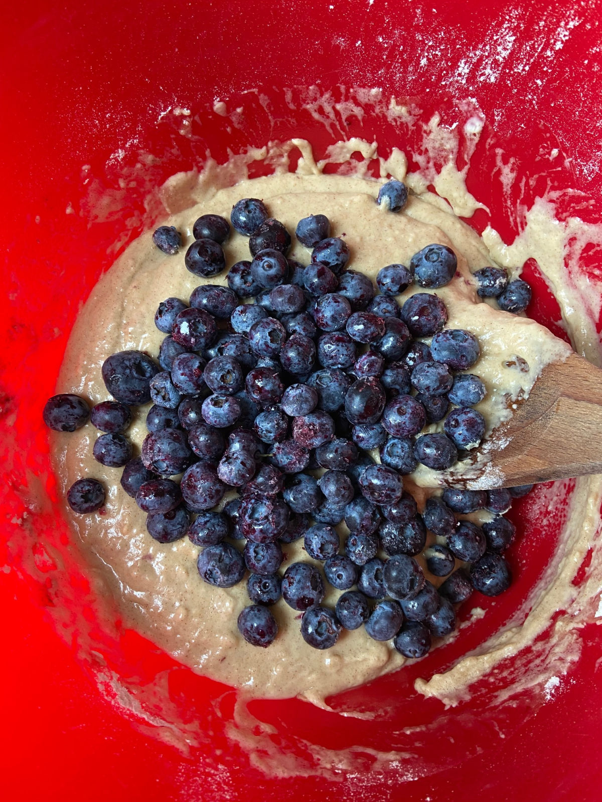 Muffin batter in a red bowl with blueberries. 