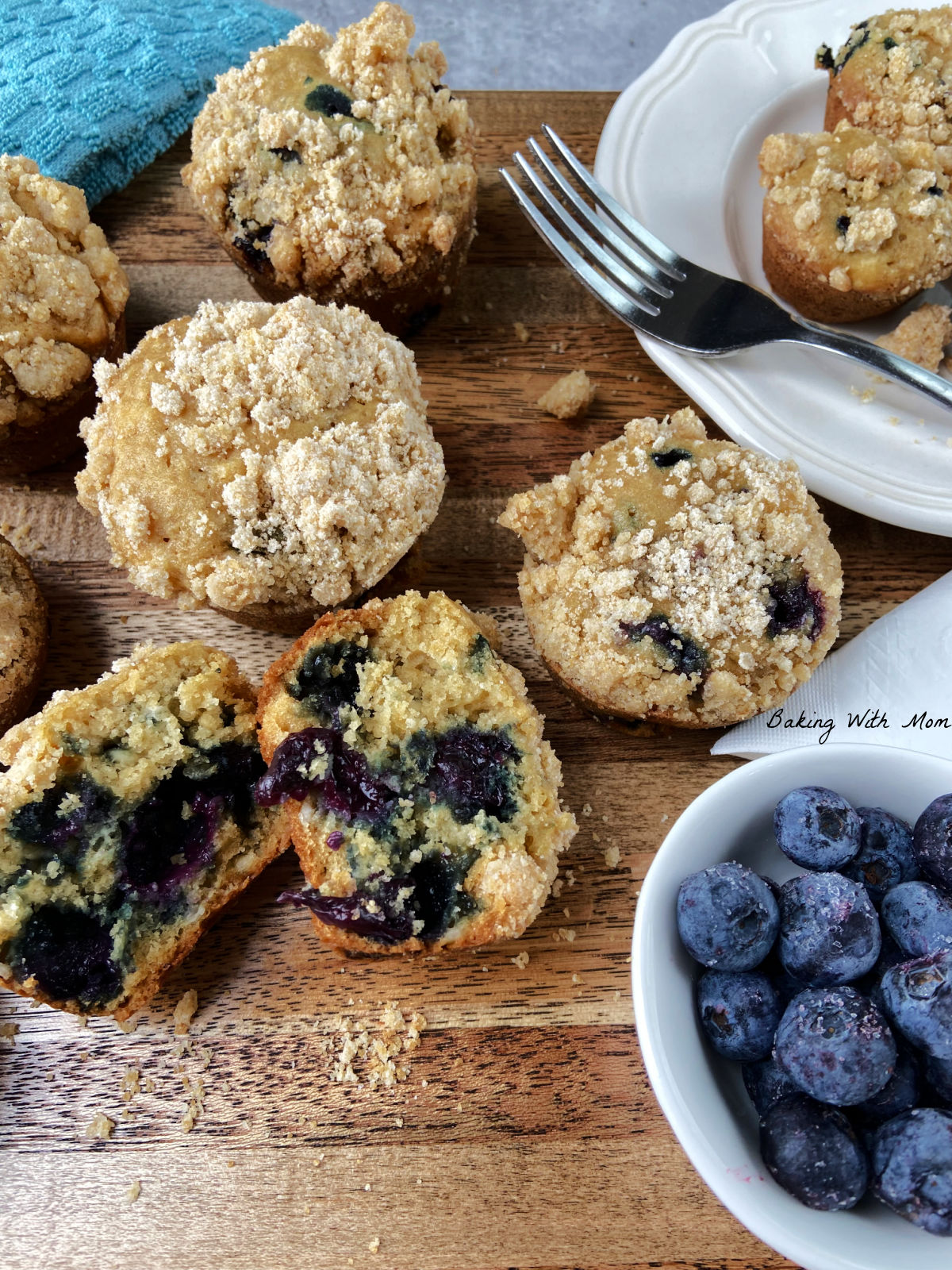 Blueberry muffins on a brown cutting board with blueberries in a bowl. 