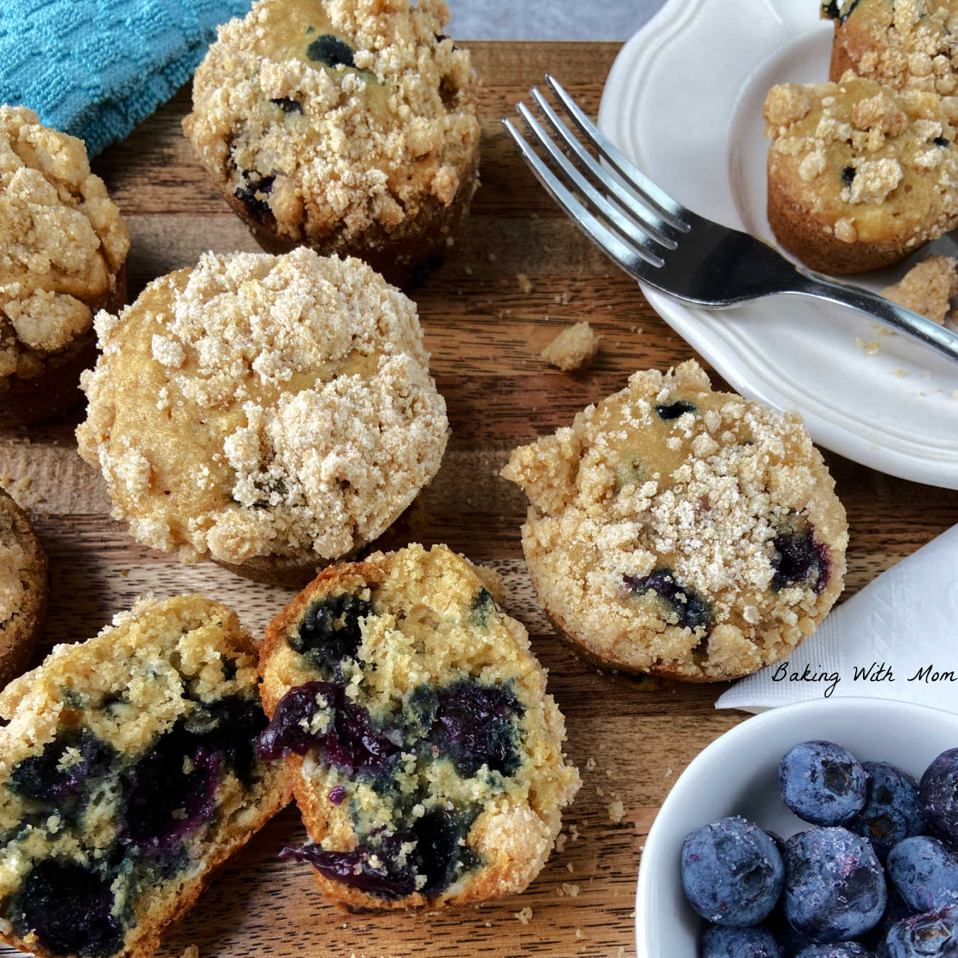 blueberry cheesecake muffins on a brown cutting board with a white plate holding muffins.