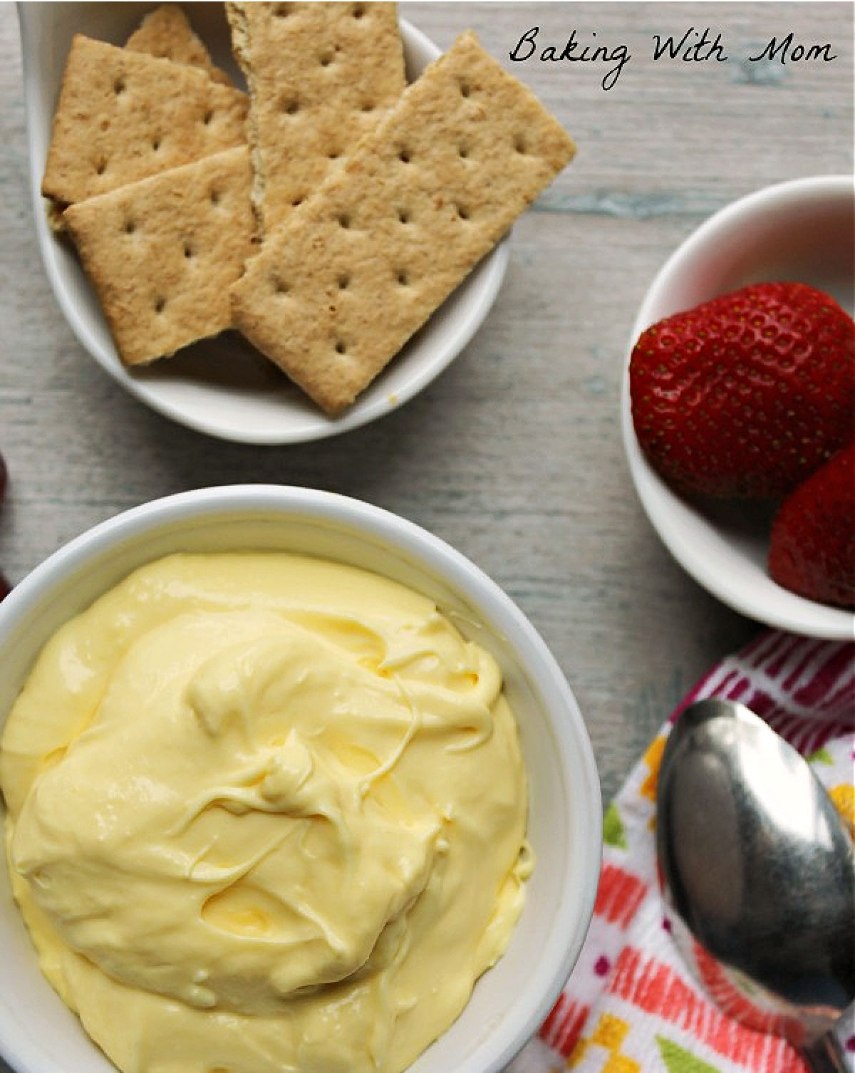 French vanilla dip in a white bowl with a spoon laying besides, crackers and strawberries. 