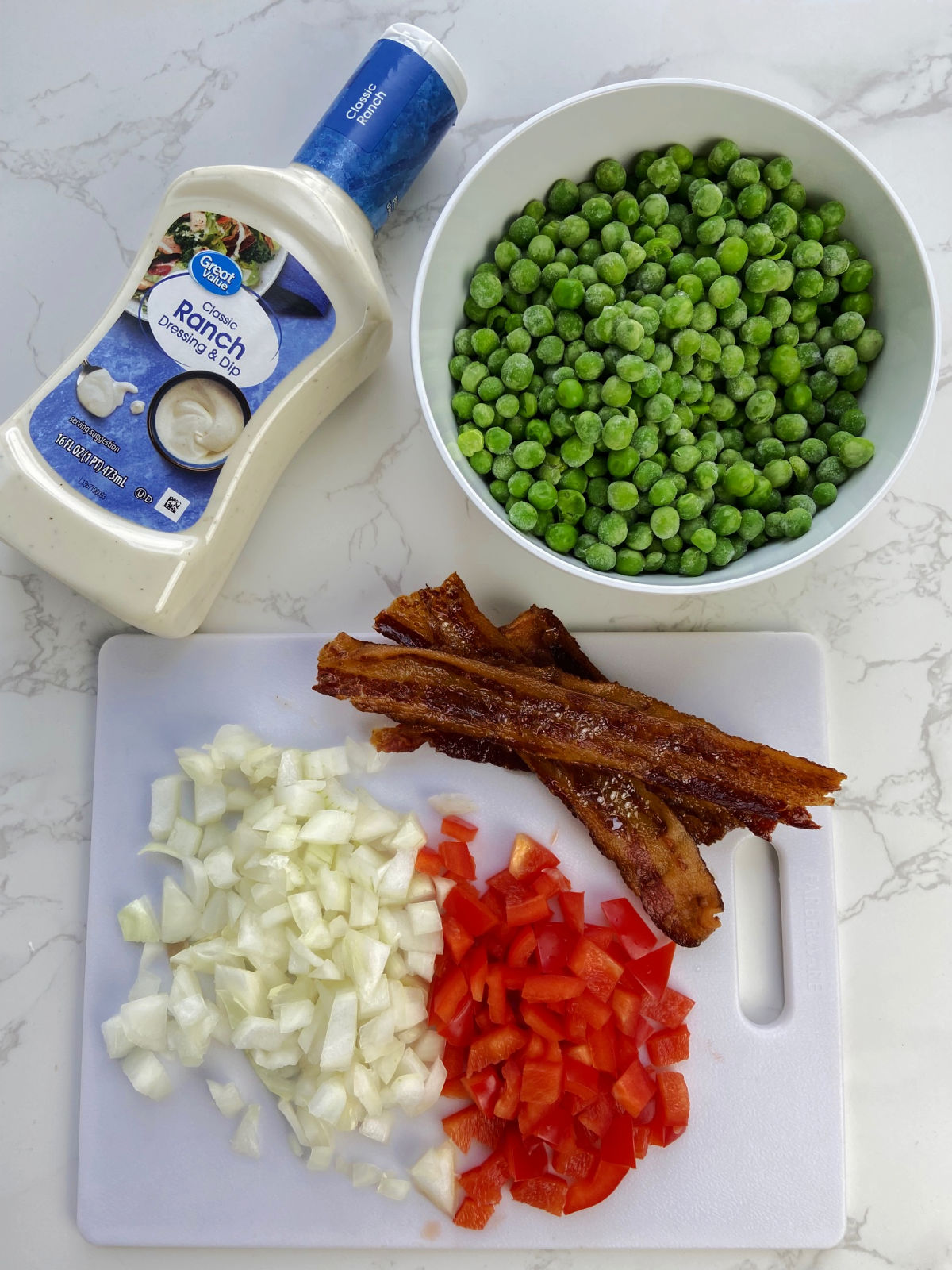 onions, peppers, bacon, peas and ranch dressing on a cutting board and laying besides. 