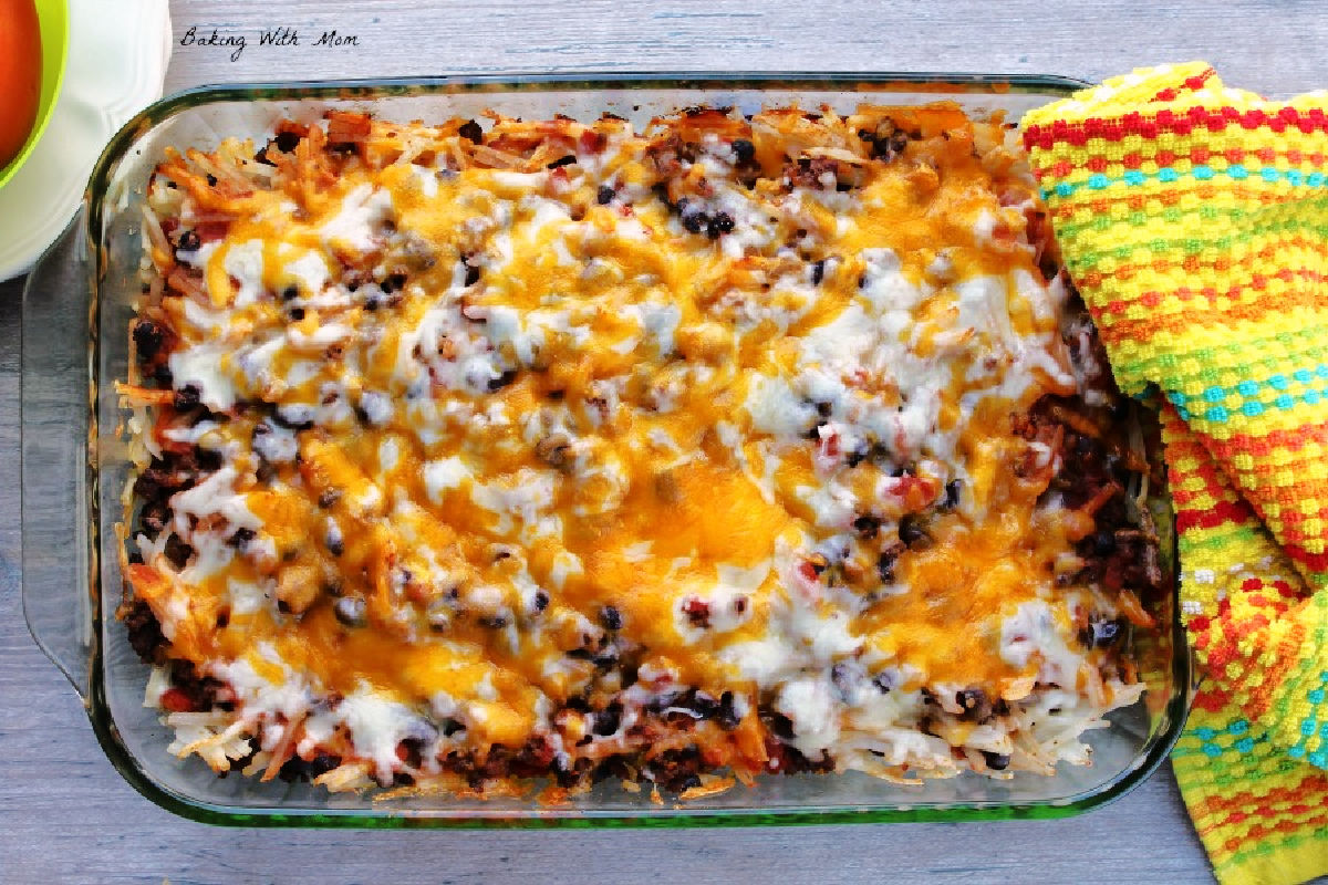 taco hashbrown casserole in a baking dish with a colored towel laying besides. 