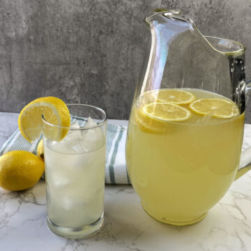Homemade lemonade in a pitcher and clear glass with ice and a lemon.
