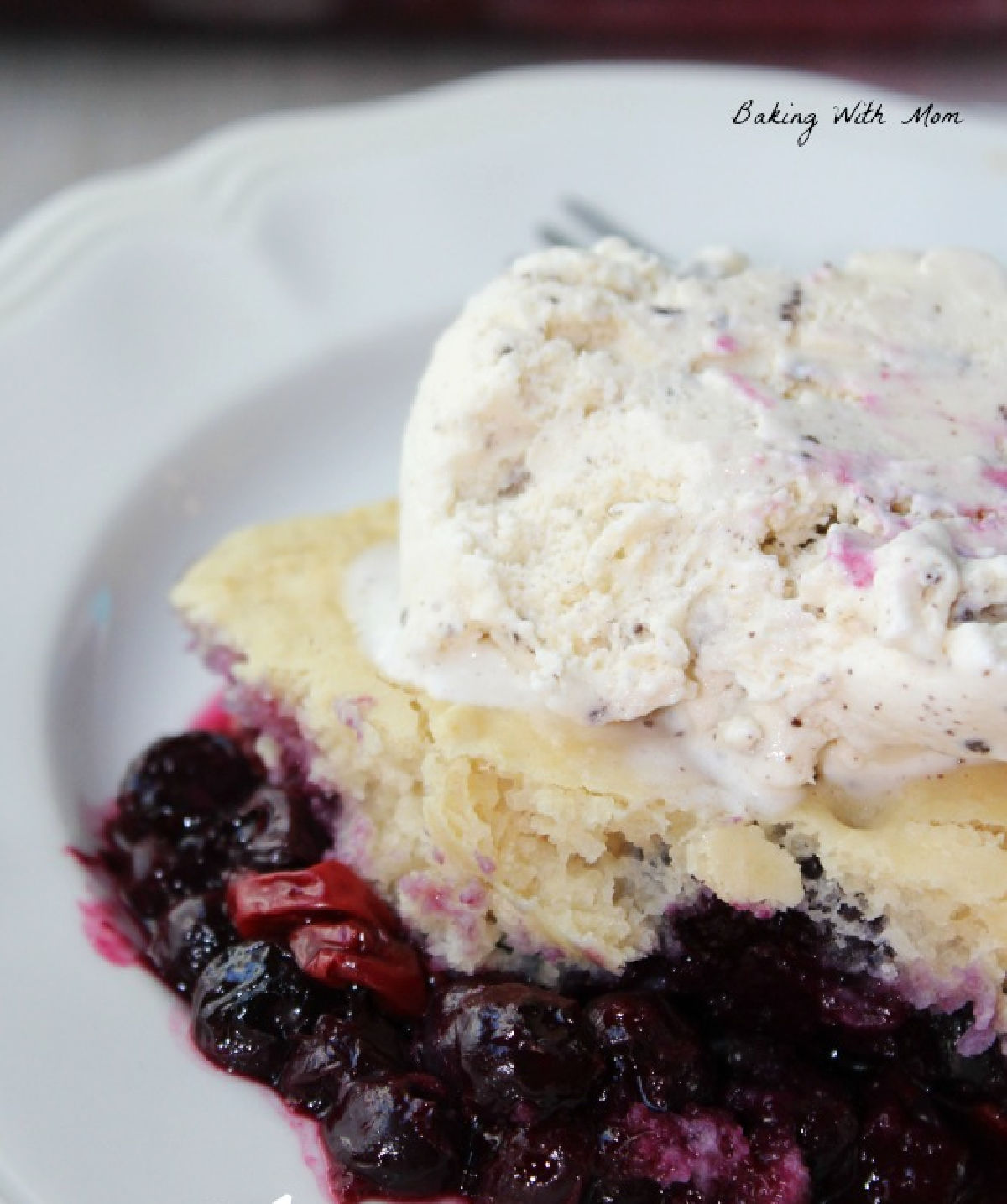 Blueberry cobbler on a white plate with ice cream on top. 