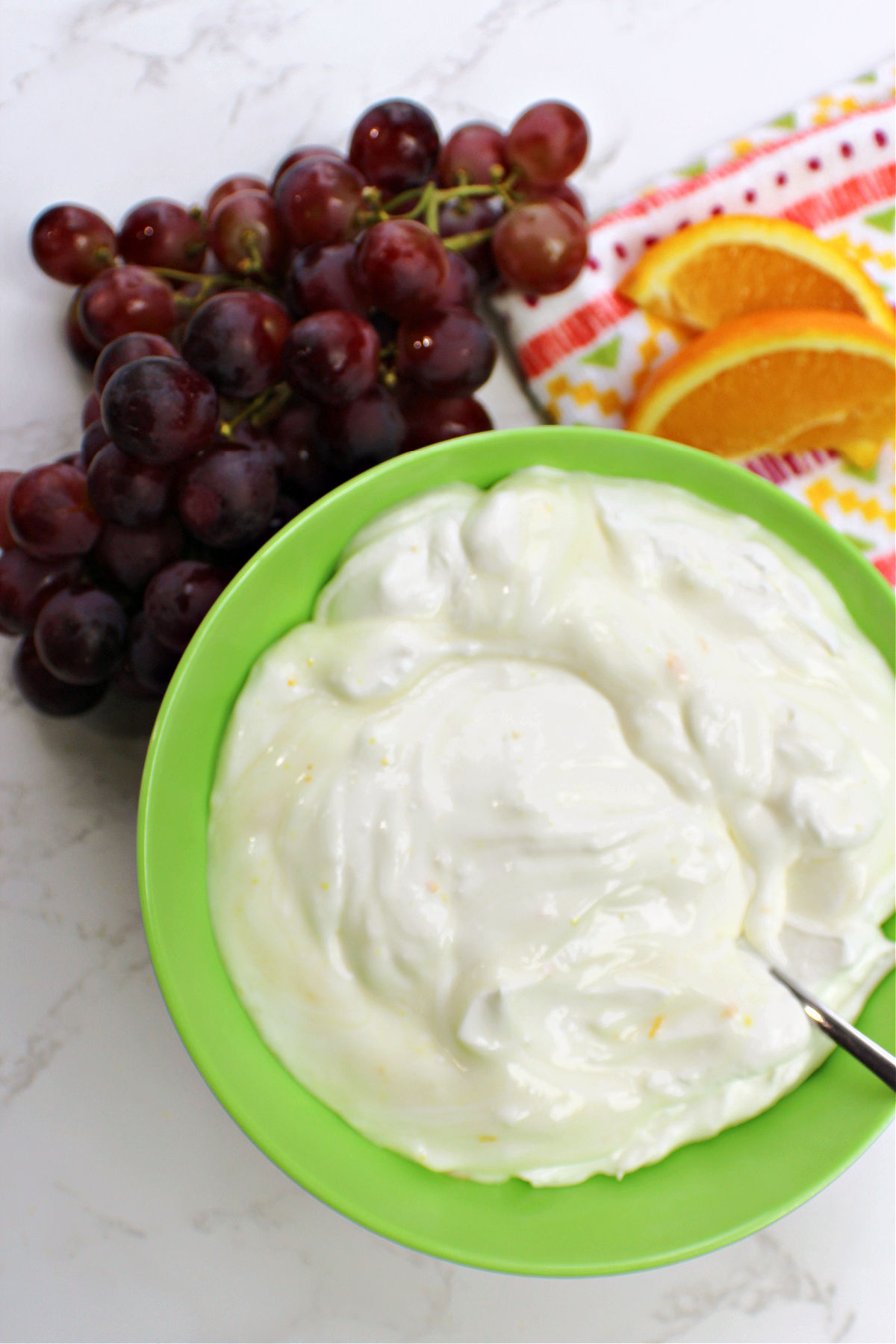 Orange dip in a green bowl with grapes and oranges. 